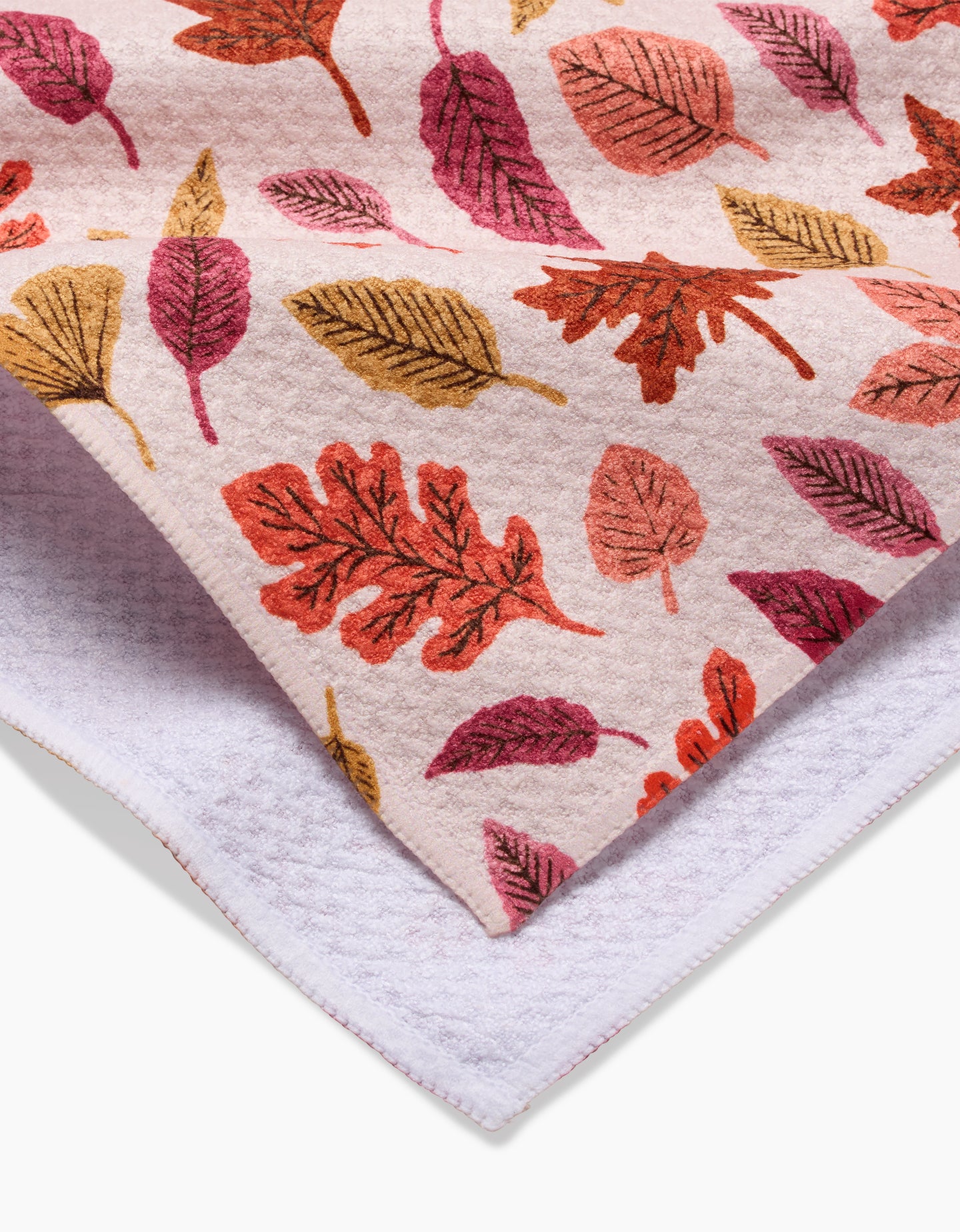 The Kayla Ann Fall Leaves dish towel is soft, absorbent, and eco-friendly with a vibrant red, orange, and yellow autumn leaf pattern on a light background, layered over a white textured towel—perfect for your kitchen.