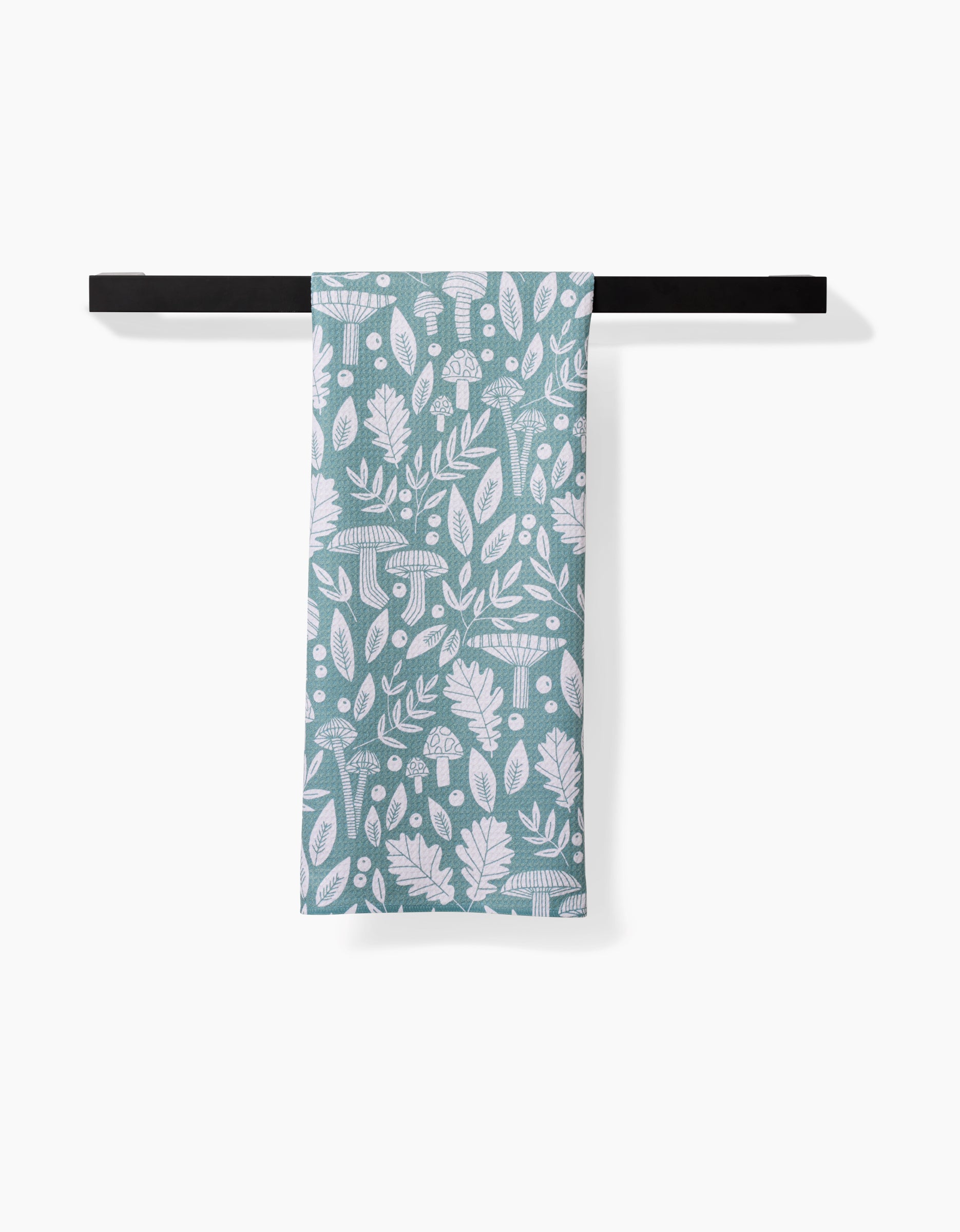 The Claire Iglesias Fall Mushrooms And Leaves green and white kitchen tea towel, featuring a leafy and mushroom pattern and made from recycled materials, hangs neatly on a black towel bar against a white background.