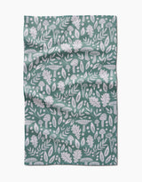 The Fall Mushrooms And Leaves tea towel by Claire Iglesias features a green background with white patterns of leaves, acorns, mushrooms, and botanical elements, shown with visible folds and creases.