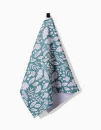 The Claire Iglesias Fall Mushrooms And Leaves kitchen tea towel, crafted from recycled materials, features a white botanical pattern of leaves and acorns on green and hangs by a black loop against a plain white background.