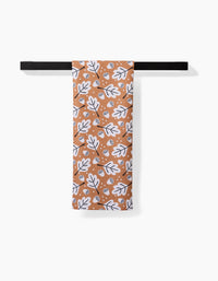 A Charlie Rowan Designs Falling Acorns tea towel featuring a white and black leaf and acorn pattern hangs neatly on a black towel bar against a white background.