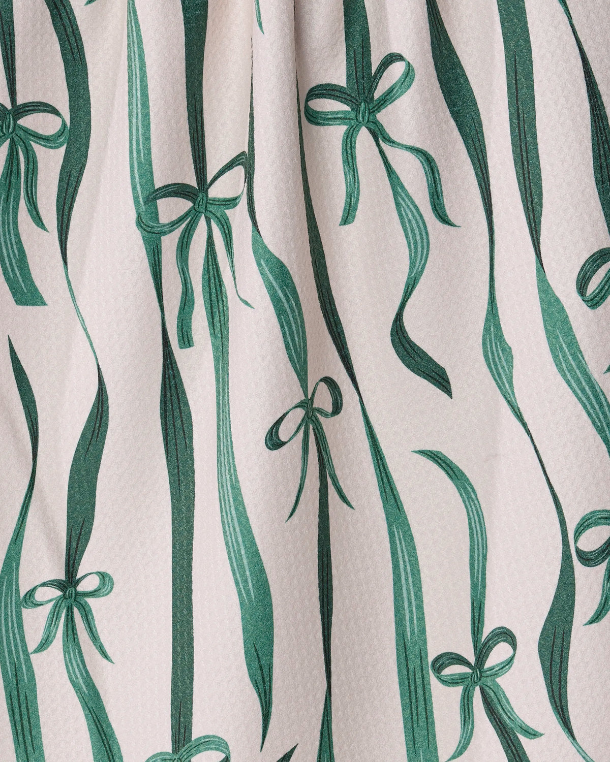 Introducing the Falling Ribbon tea towel by Geometry: Crafted from recycled materials, this ultra-absorbent towel features a white fabric adorned with varying widths of vertical green ribbons that gently wave across its surface, accented by bows tied at irregular intervals. Both stylish and sustainable, it’s the perfect charming addition to any kitchen.