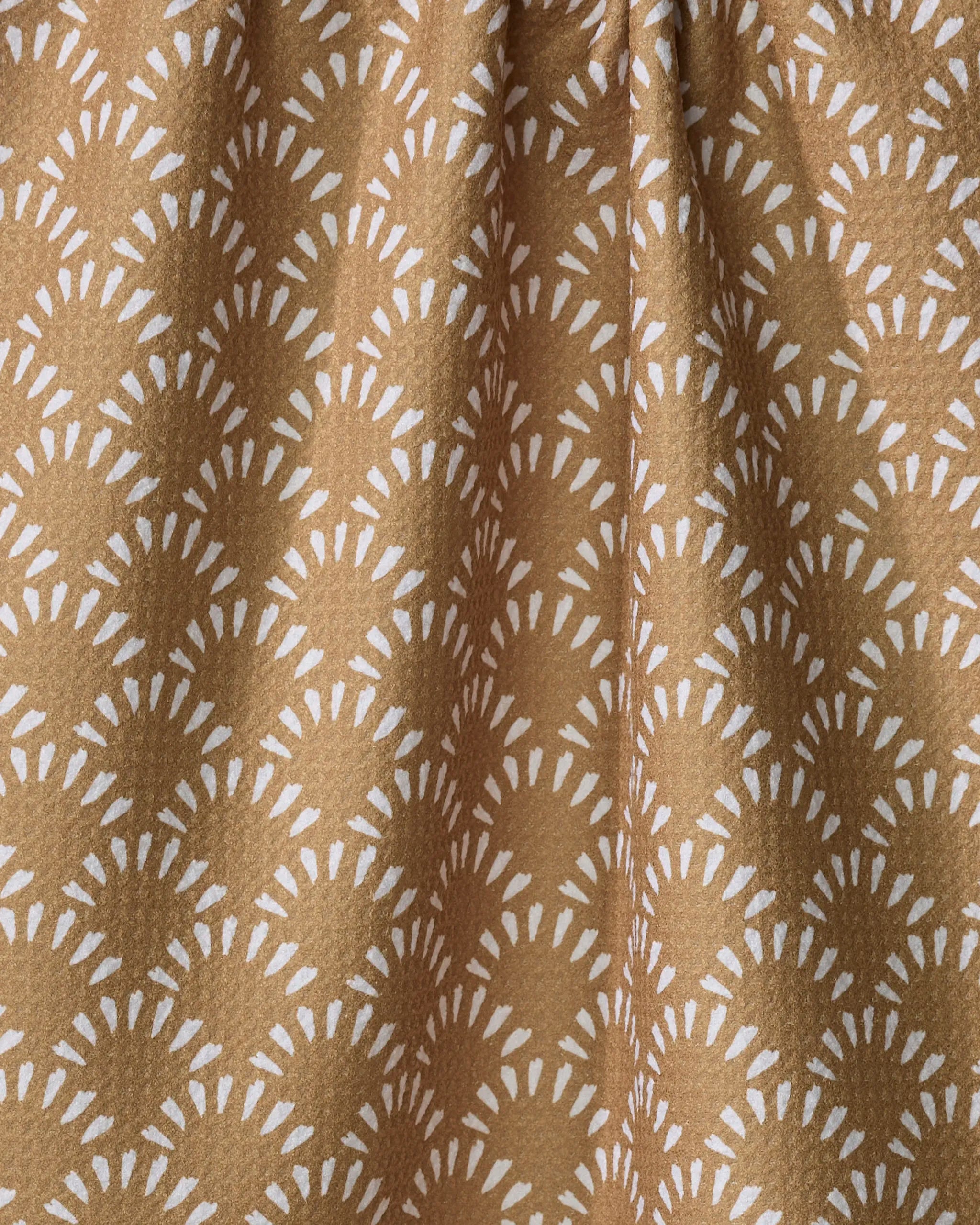 A close-up of Hufton Studio's Fantail recycled kitchen towel shows brown fabric with a white sunburst-like geometric pattern, softly gathered to create gentle folds and shadows.
