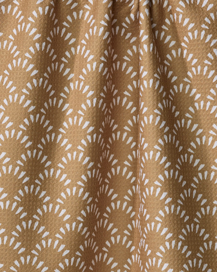 A close-up of Hufton Studio's Fantail recycled kitchen towel shows brown fabric with a white sunburst-like geometric pattern, softly gathered to create gentle folds and shadows.