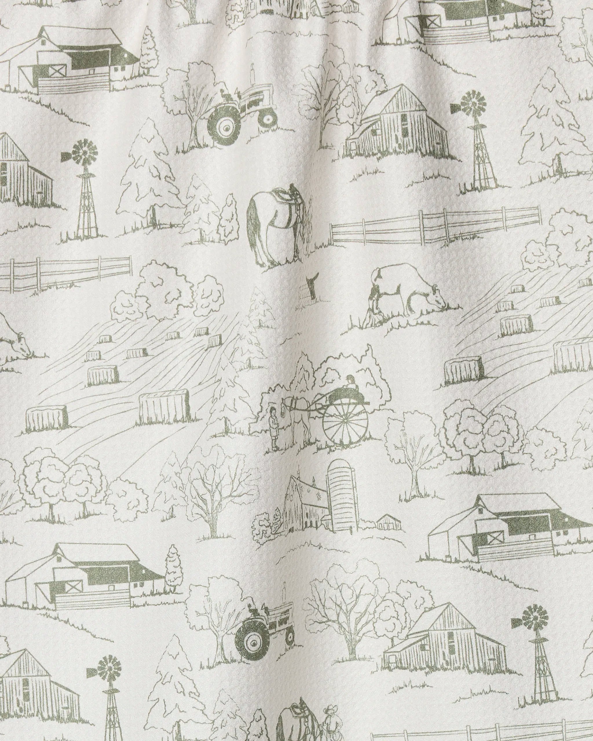 The "Farmyard" tea towel by Hannah Langford features green line drawings of barns, tractors, trees, cows, and windmills on a cream background—perfect as a quick-drying, charming addition to your kitchen.