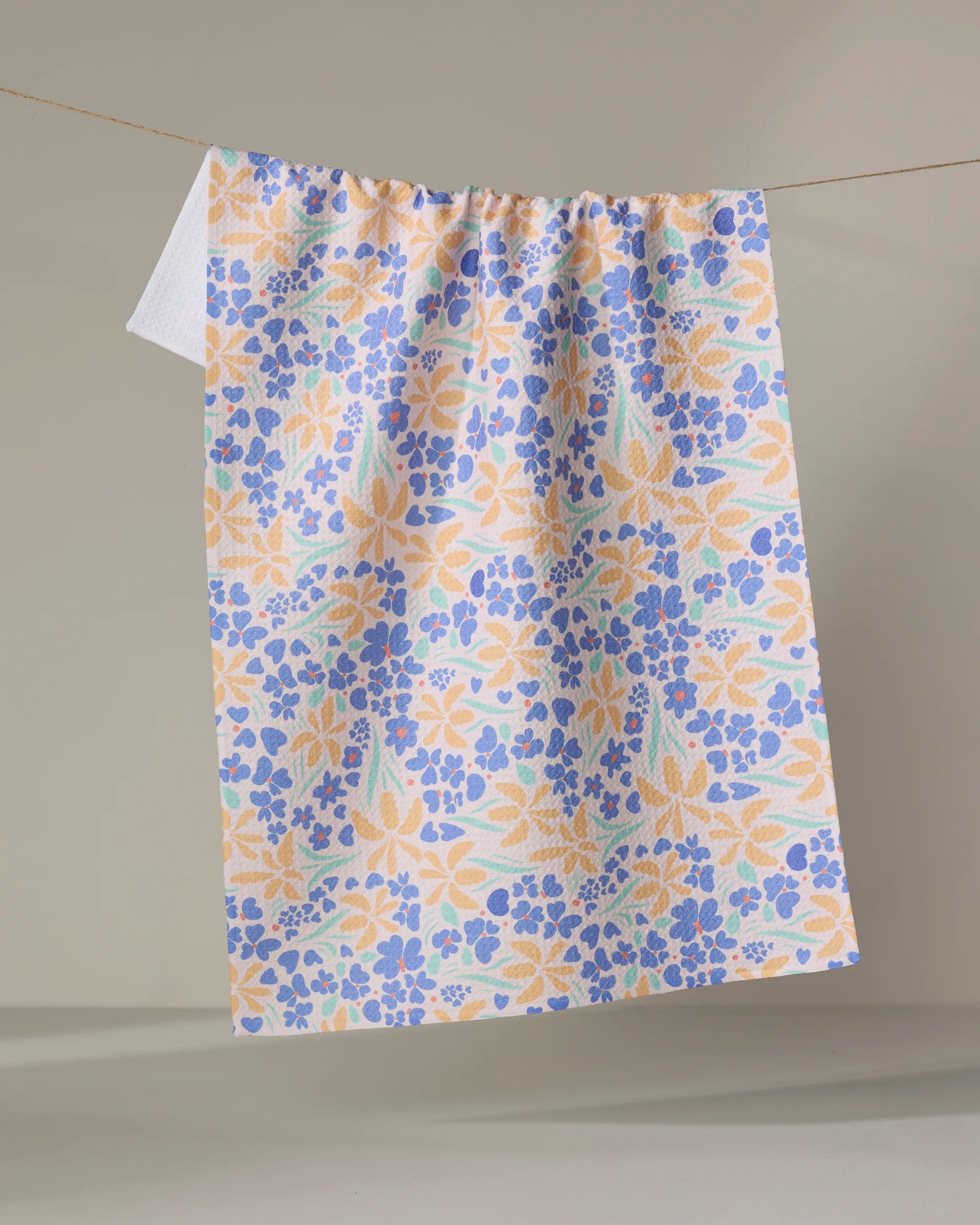 The February tea towel by Elisabeth Wing features a colorful floral pattern in blue, yellow, and light orange, displayed against a plain background.