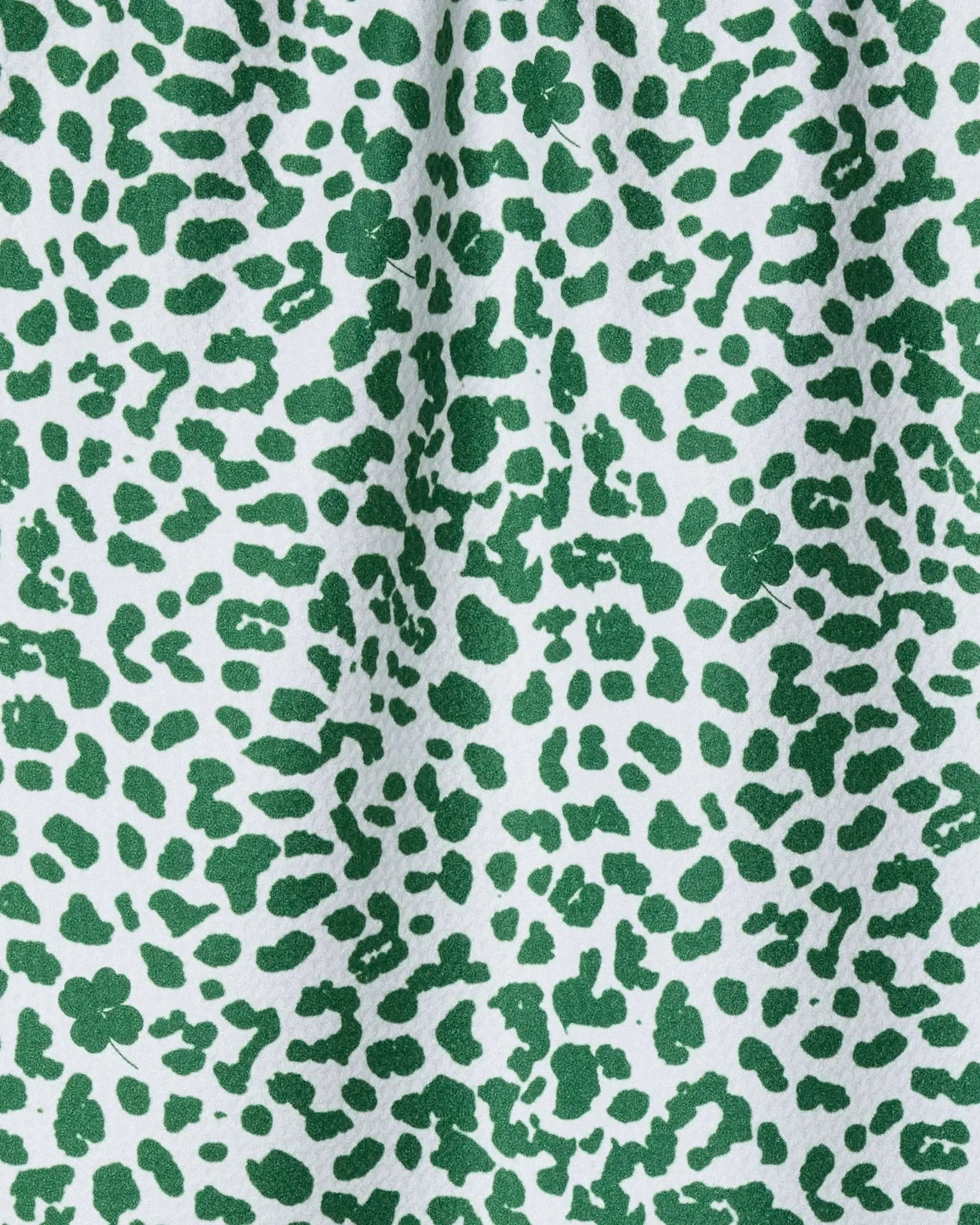 The Geometry Feroz tea towel features a green abstract leopard print on white, made from recycled materials. Visible folds and shadows accentuate its ultra-absorbent, slightly wrinkled fabric.