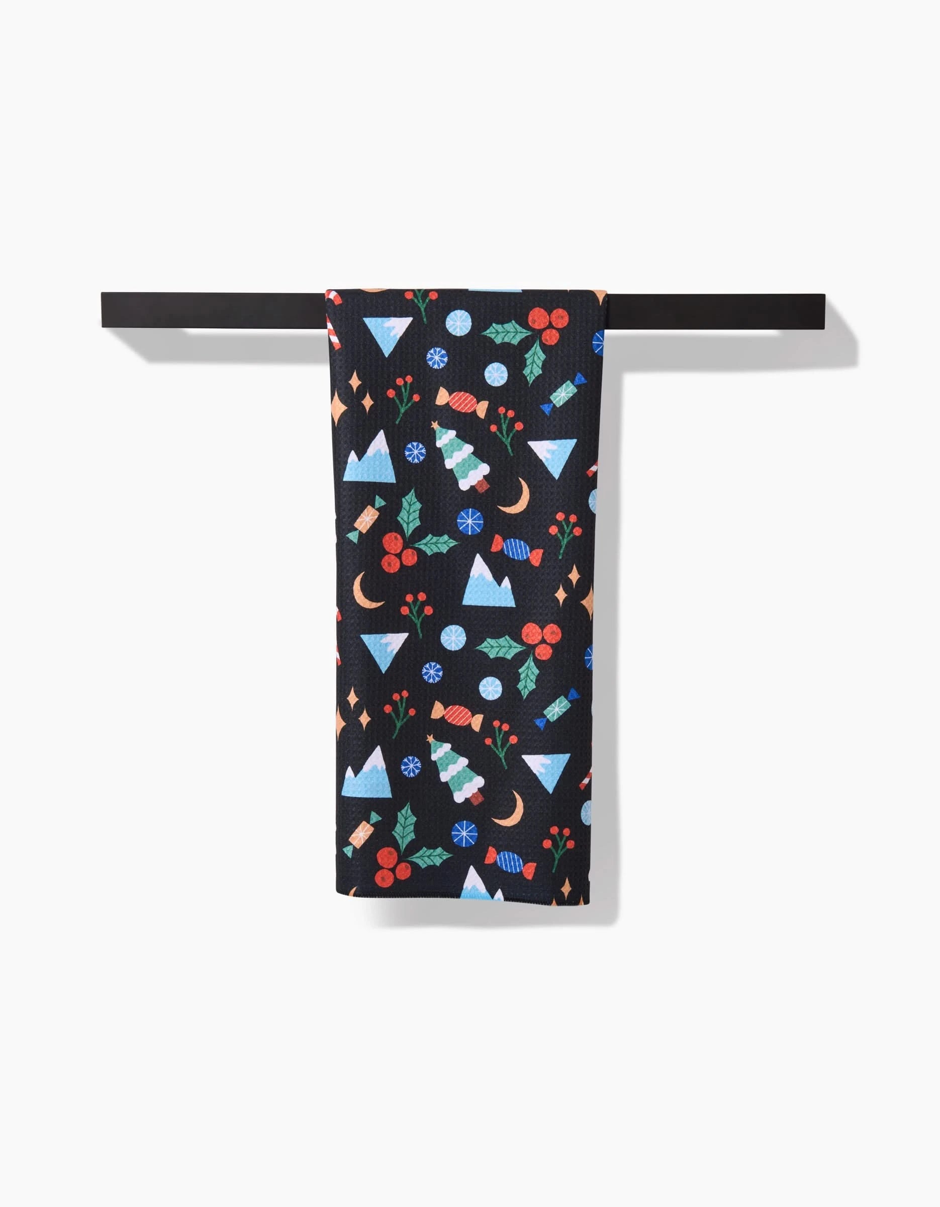 The Claire Iglesias Festive Christmas tea towel features colorful geometric holiday patterns on black and hangs neatly on a horizontal bar. Made from ultra-absorbent recycled materials.