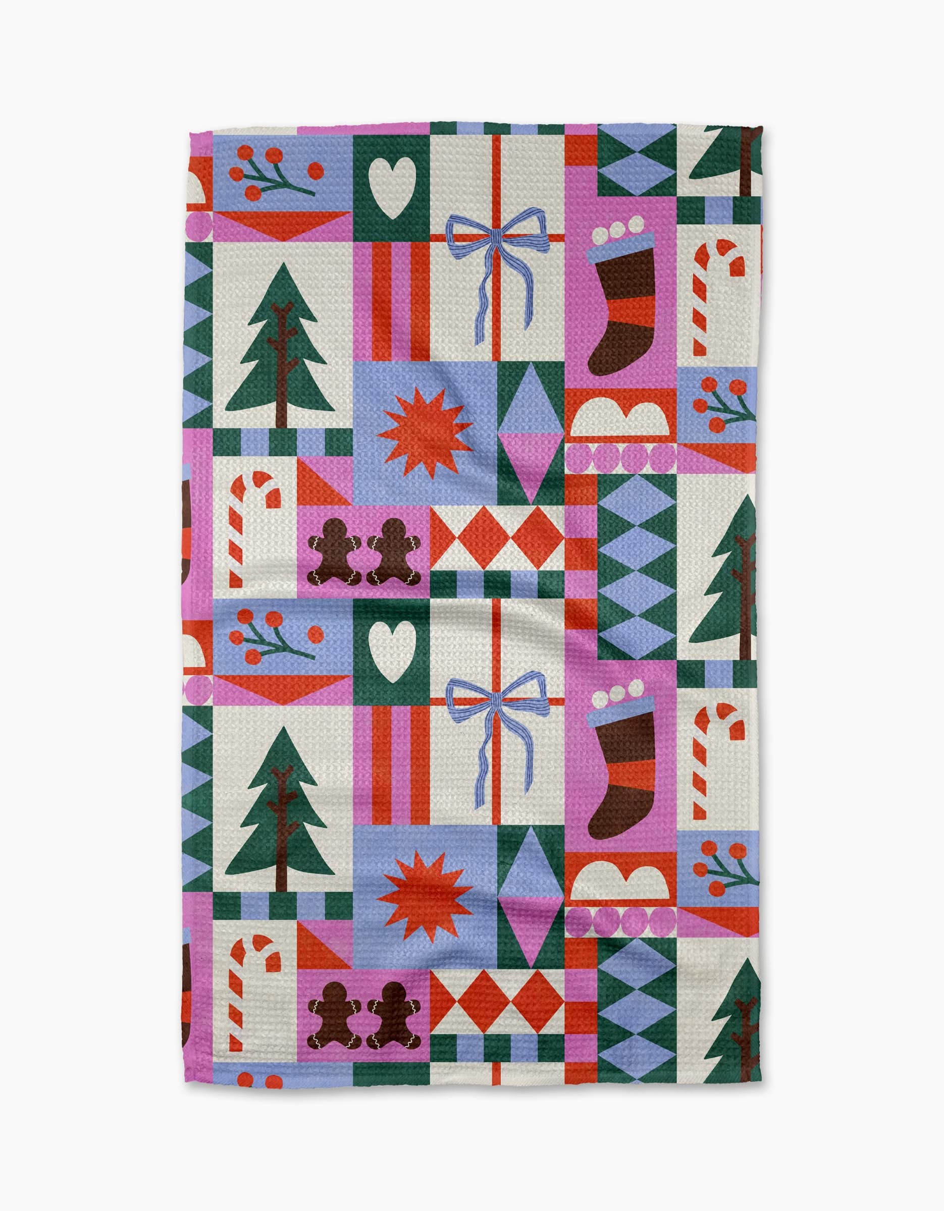 The Claire Iglesias Festive Christmas Quilt tea towel features a colorful patchwork of trees, candy canes, stockings, hearts, and more in red, green, purple, and blue—crafted from quick-drying recycled materials.