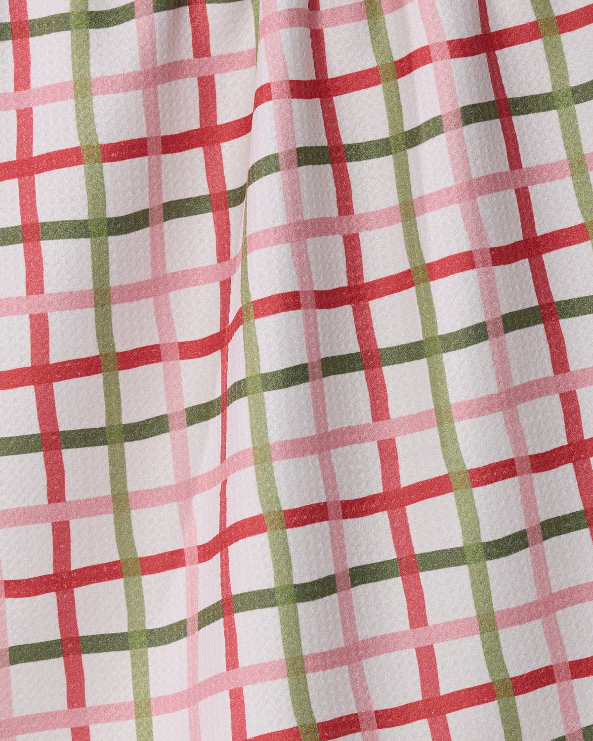 A close-up of the Festive Plaid tea towel by Geometry shows its textured fabric featuring intersecting red, pink, and green lines on a white background; this ultra-absorbent towel is crafted from recycled materials.