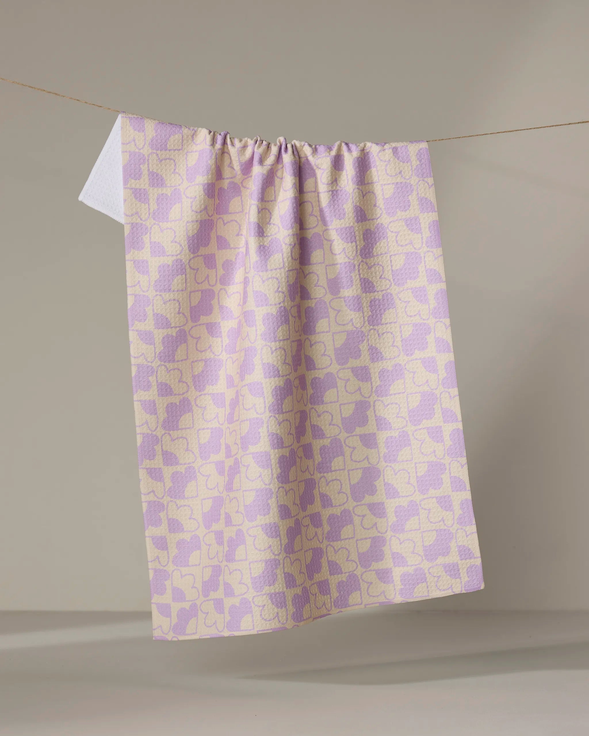 The Field Day recycled kitchen towel by Beetle Ink Co., featuring a pastel pink and yellow butterfly pattern, hangs on a line against a plain neutral background.