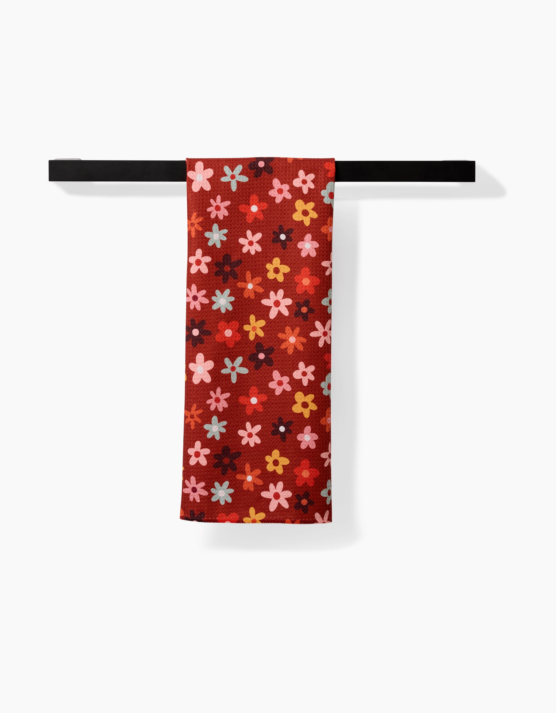The Sara Mari Field Of Fall Daisies towel, featuring a vibrant red base with pink, yellow, blue, and black floral patterns, hangs on a black towel bar against a white background.