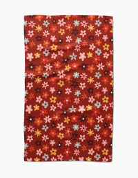 The Sara Mari Field Of Fall Daisies is a rectangular red tea towel with a pattern of small, colorful flowers in pink, yellow, blue, and orange evenly distributed across the surface.