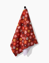 The Sara Mari Field Of Fall Daisies kitchen towel features colorful pink, yellow, orange, and brown floral patterns. Crafted from recycled materials, it hangs from a black loop and adds a vibrant touch to your kitchen décor.