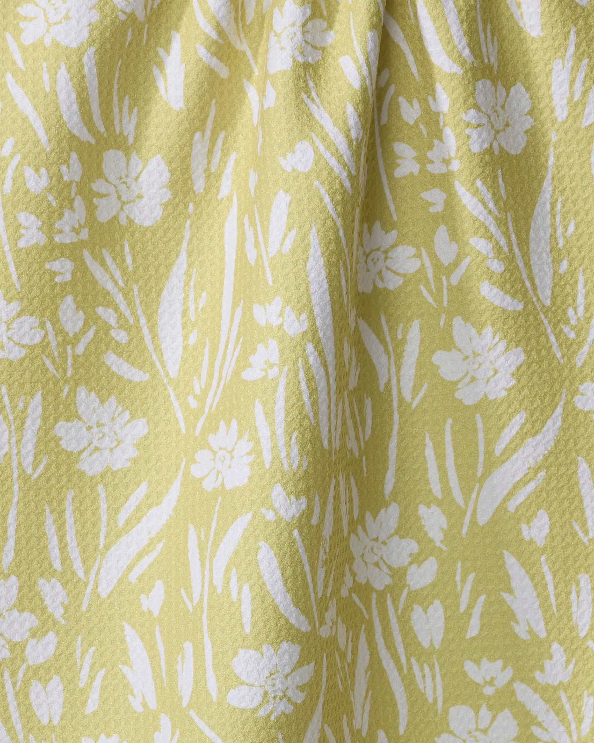 Field of Wildflowers by Ashley Celena is a yellow tea towel with a textured surface and white floral pattern. Made from recycled materials, it features soft gathers that create gentle folds and shadows.
