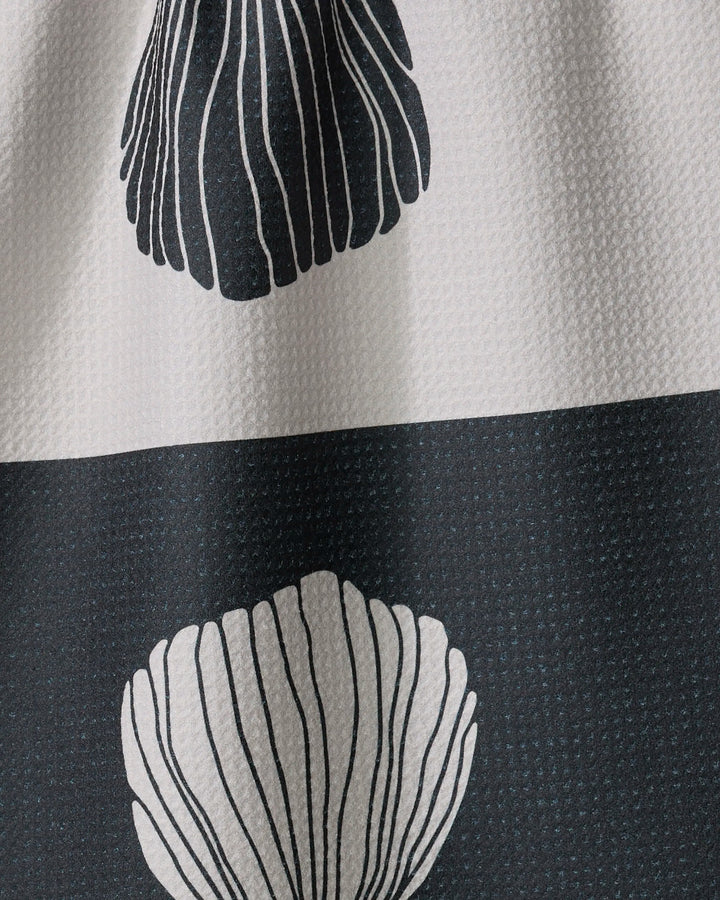 A close-up of the Anna Christian Fika tea towel, showcasing its textured fabric with white and dark gray stripes and large, stylized shell or leaf motifs outlined in fine lines.