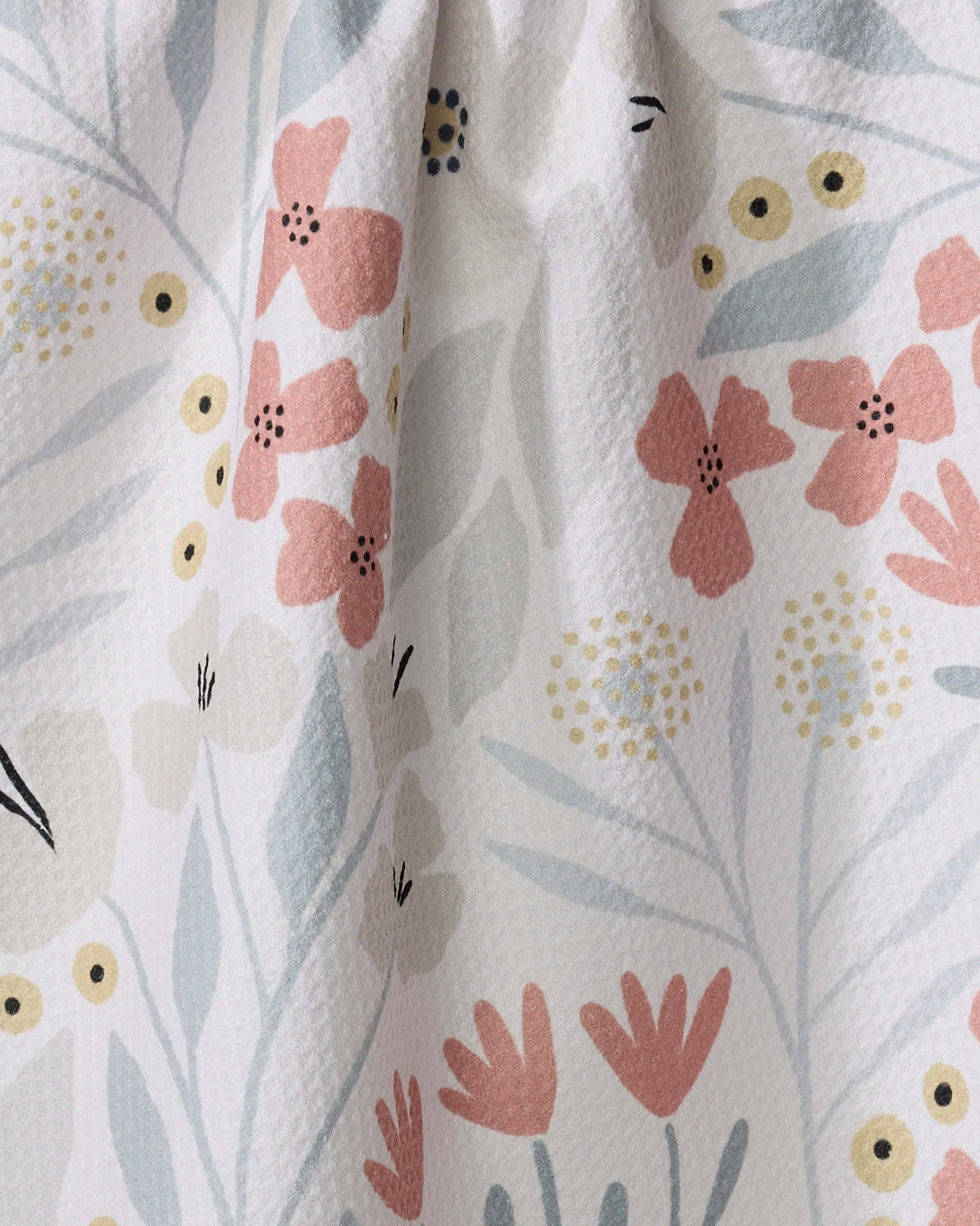 The Fiona Cream tea towel by Amy MacCready features textured white fabric with pink, yellow, and beige floral patterns, blue-gray leaves, and small yellow circles. This quick-drying towel is slightly gathered at the top.