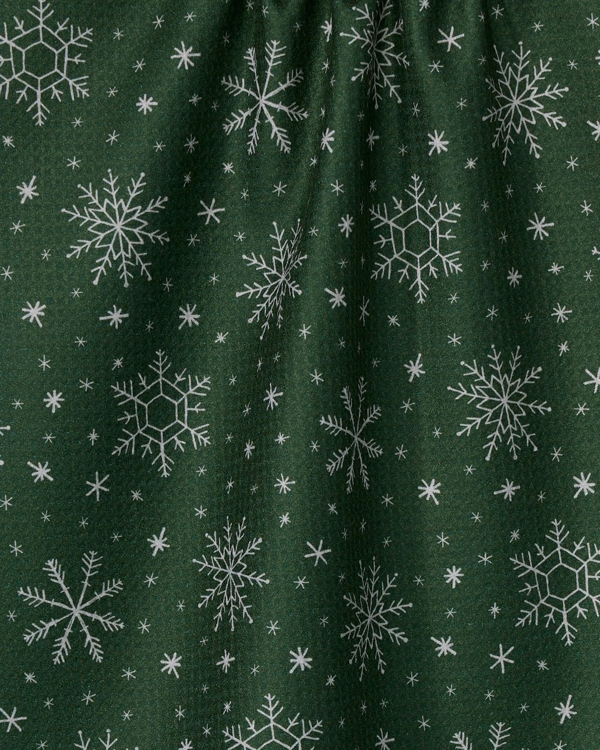 Firlight by Geometry: a dark green tea towel made from recycled materials, adorned with white snowflakes of varying sizes and a slightly gathered top, blending eco-friendly design with festive winter charm.