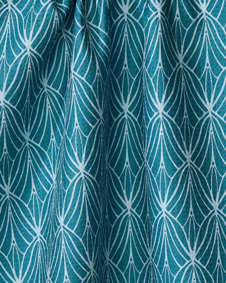 The Fish Tails tea towel by Marta Harvey features a teal fabric with a white geometric floral pattern of petal-like shapes and dots. Made from ultra-absorbent recycled materials, its gentle folds add textured shadows.