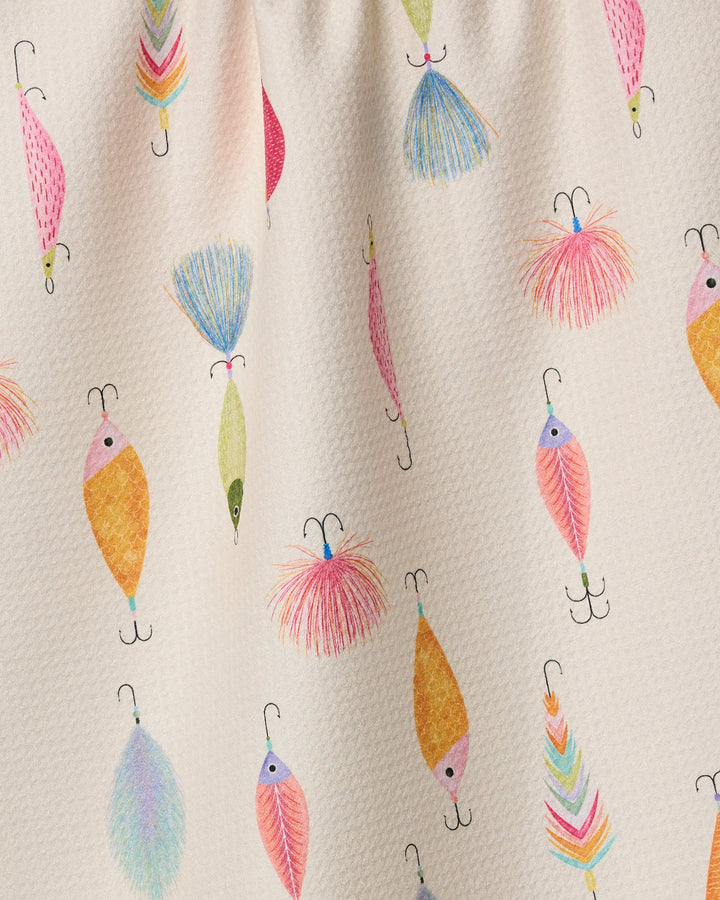 A close-up of Geometry's Fishing Lures tea towel, made from recycled materials and featuring colorful pink, blue, yellow, and orange fishing lure patterns on a light cream background.