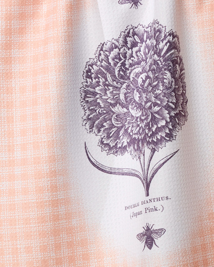 A close-up of Geometry's Fleur et Abeille kitchen tea towel, made from recycled materials, with a peach and white checkered pattern, a detailed double dianthus flower and bee illustration, and the text DOUBLE DIANTHUS. (Japan Pink.).