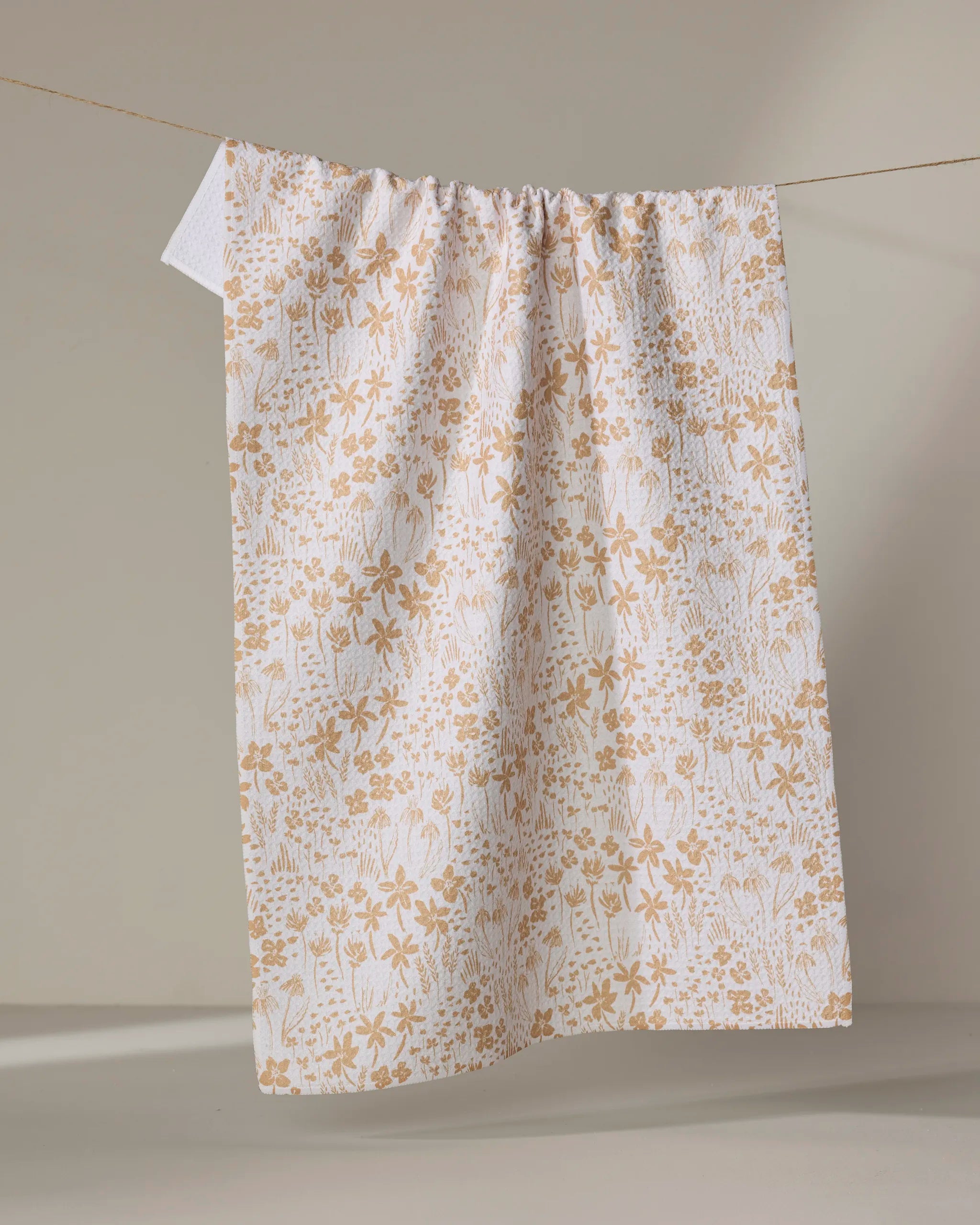 The Hufton Studio "Floating Meadow" recycled kitchen towel, white with a light brown floral botanical pattern, hangs from a string against a neutral background.