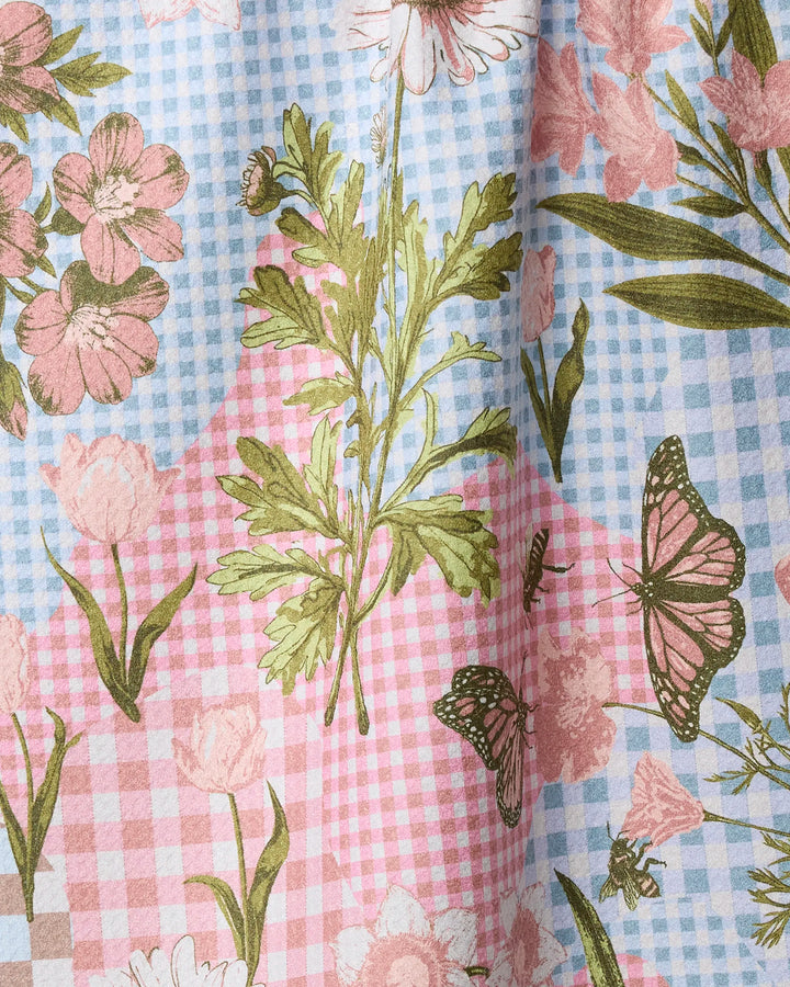 The Geometry "Floral Collage" tea towel features a pastel blue and pink gingham design with printed green leaves, pink flowers, a butterfly, and a bee—crafted from recycled materials for eco-friendly style.