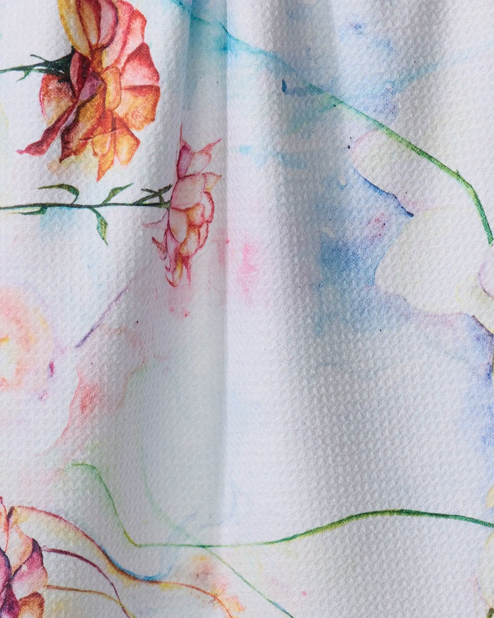A close-up of Floral Landscape by Stefanie Bales shows textured white fabric from recycled materials with a watercolor floral pattern—orange and pink flowers, green stems, and pastel blue/yellow strokes—ideal for a stylish tea towel.
