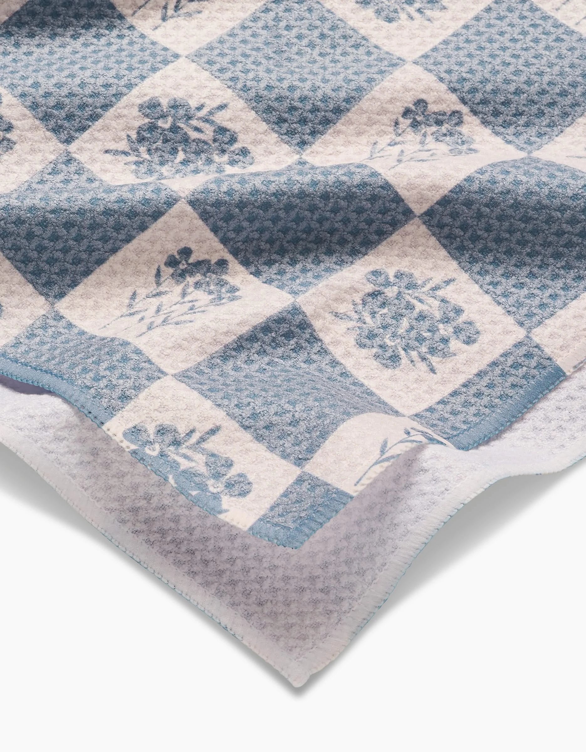 A close-up of the Floral Patchwork tea towel by Charlie Rowan Designs, featuring blue and white checks with floral details, a scalloped edge, and crafted from recycled materials.