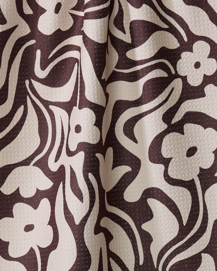 Floral Reverie by Gerdadzy features ivory floral and leaf patterns on dark brown textured fabric with abstract, flowing shapes—crafted from recycled materials for an eco-friendly, boldly decorative tea towel.