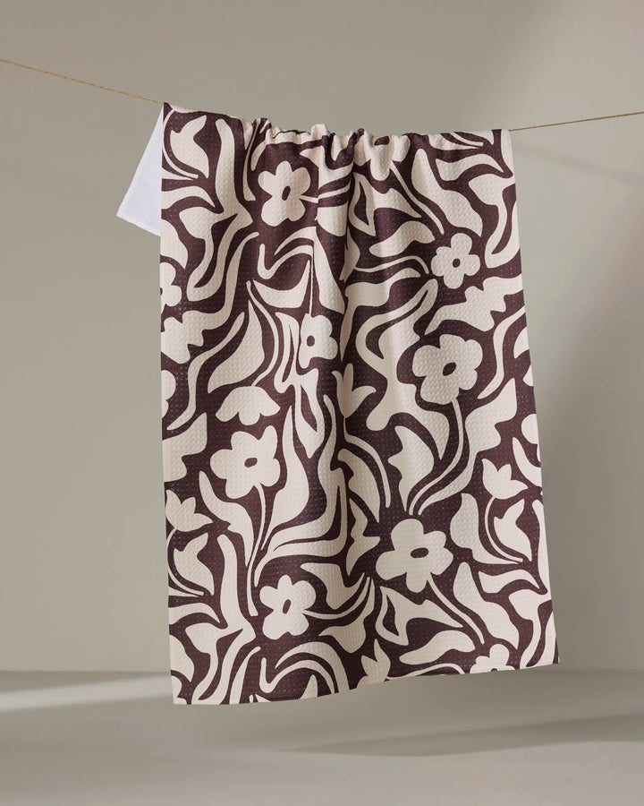 The Gerdadzy Floral Reverie kitchen towel, featuring an ultra-absorbent brown and white abstract floral design, hangs on a clothesline against a neutral background.