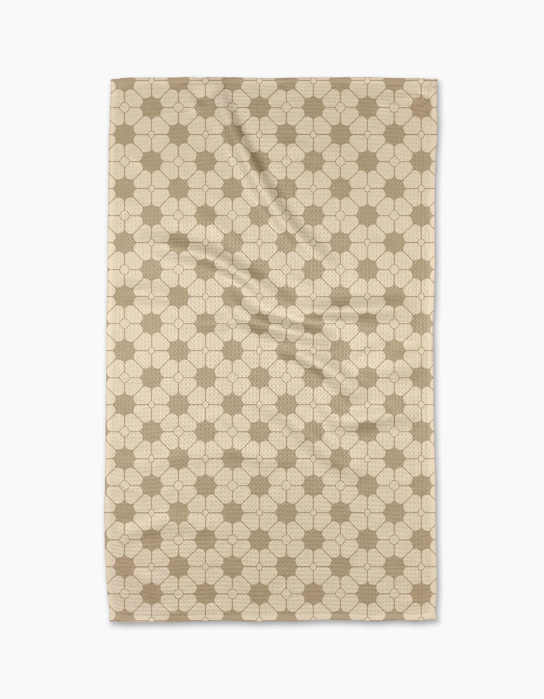 The Geometry Flora Tile Tea Towel is a beige rectangular towel with a repeating hexagon and interlocking circle pattern in light brown, displayed flat on a white background. Made from premium Geoweave fabric for superior absorbency and softness.