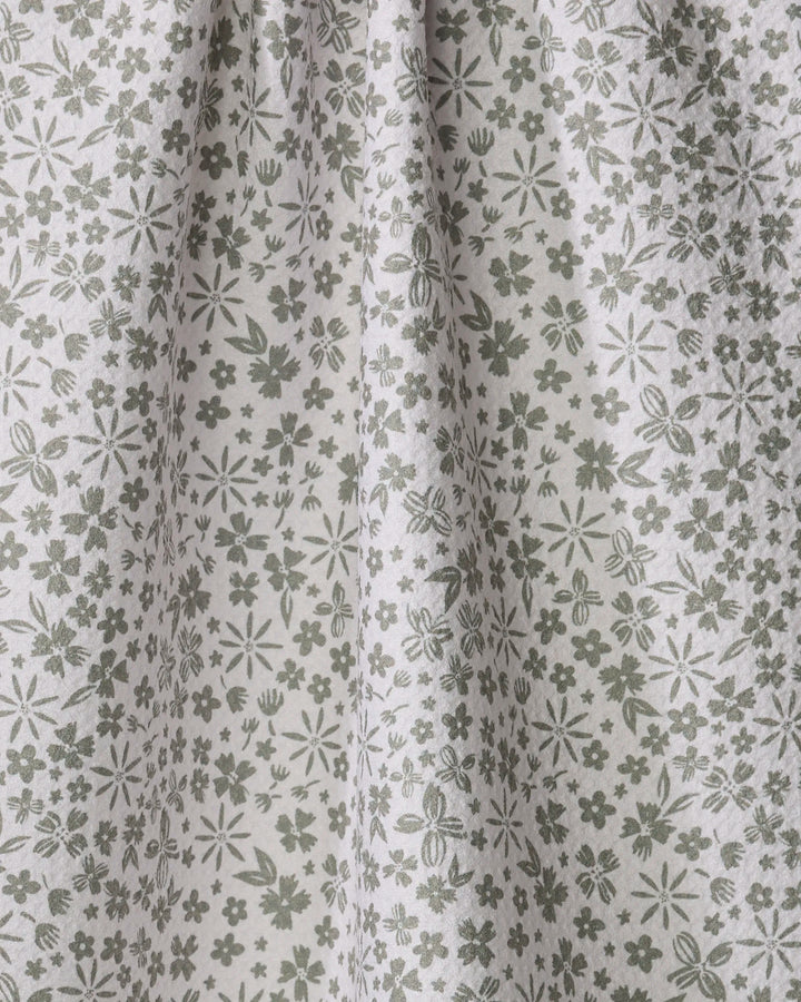 Close-up of Hufton Studio’s Flourish Gardens kitchen towel—a light, absorbent fabric with a green and white floral pattern featuring small flowers, leaves, and stems. The towel hangs softly in gentle folds.