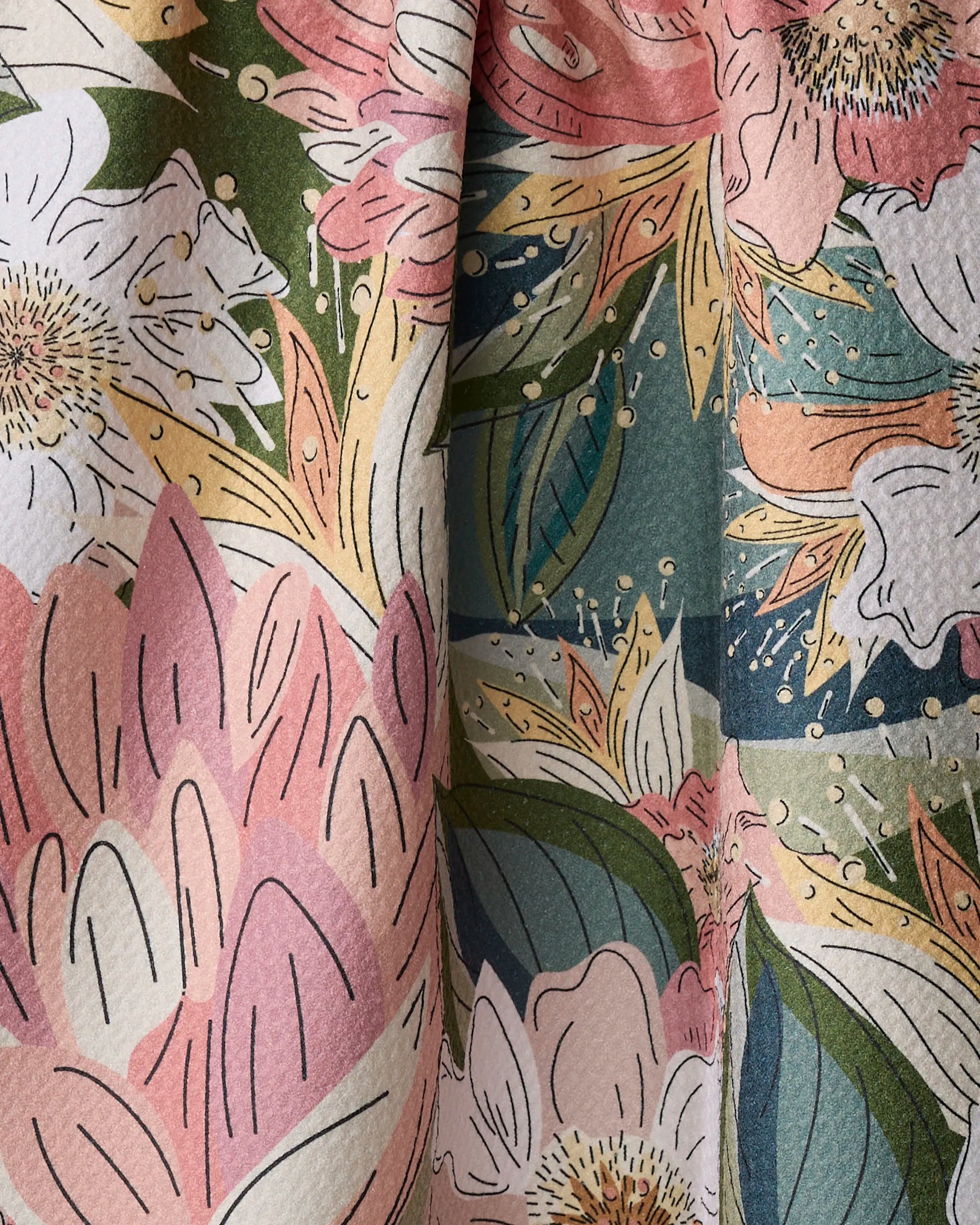 Close-up of the Flower Explosion kitchen towel by Second Nature Studio, featuring a colorful floral pattern in pink, green, white, yellow, and blue on recycled fabric with a textured surface and soft folds.