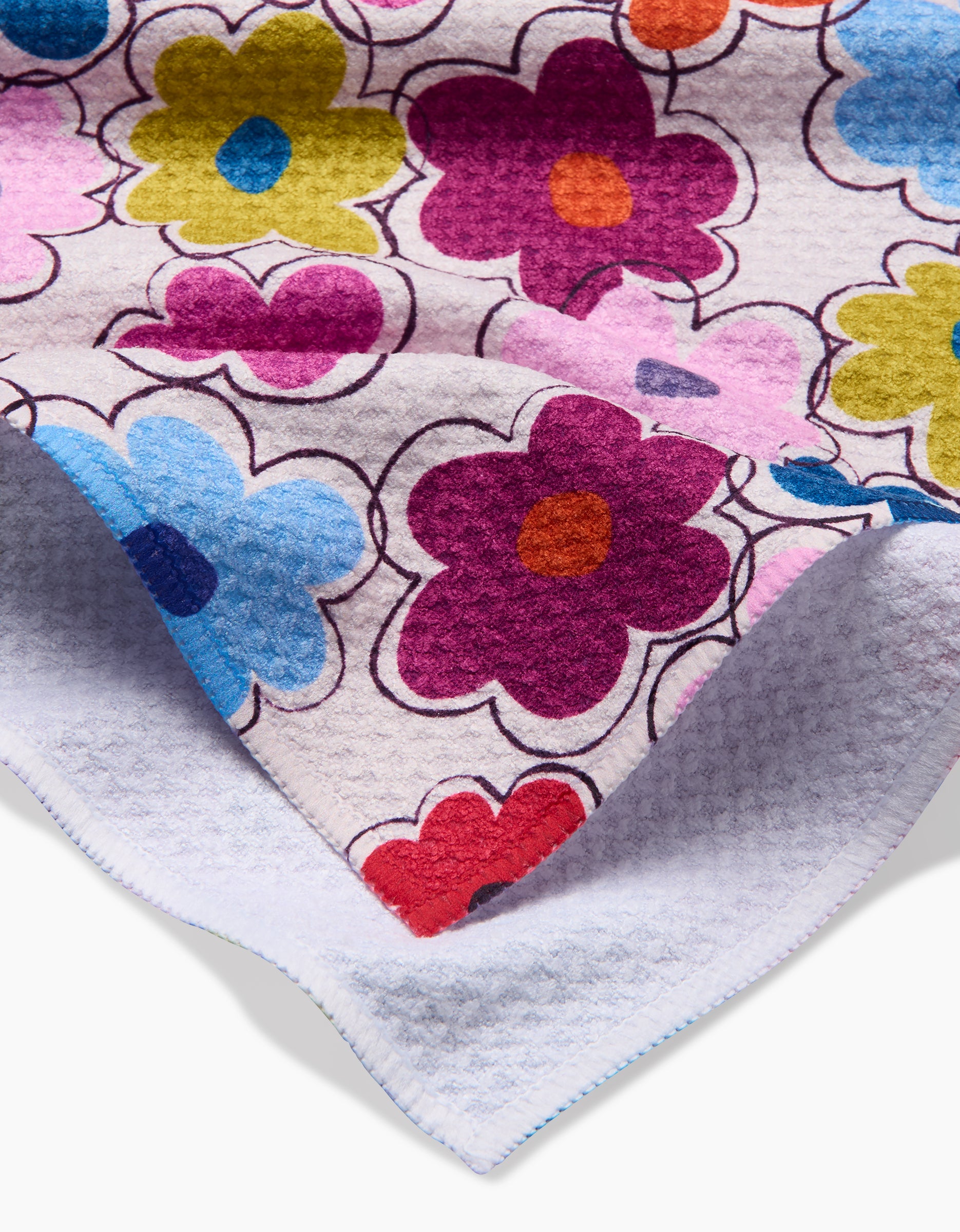A close-up of Lizzie Clark’s Flower Fling tea towel, made from soft Geoweave fabric and showcasing a vibrant, overlapping floral pattern; the white backing is visible at the corner.