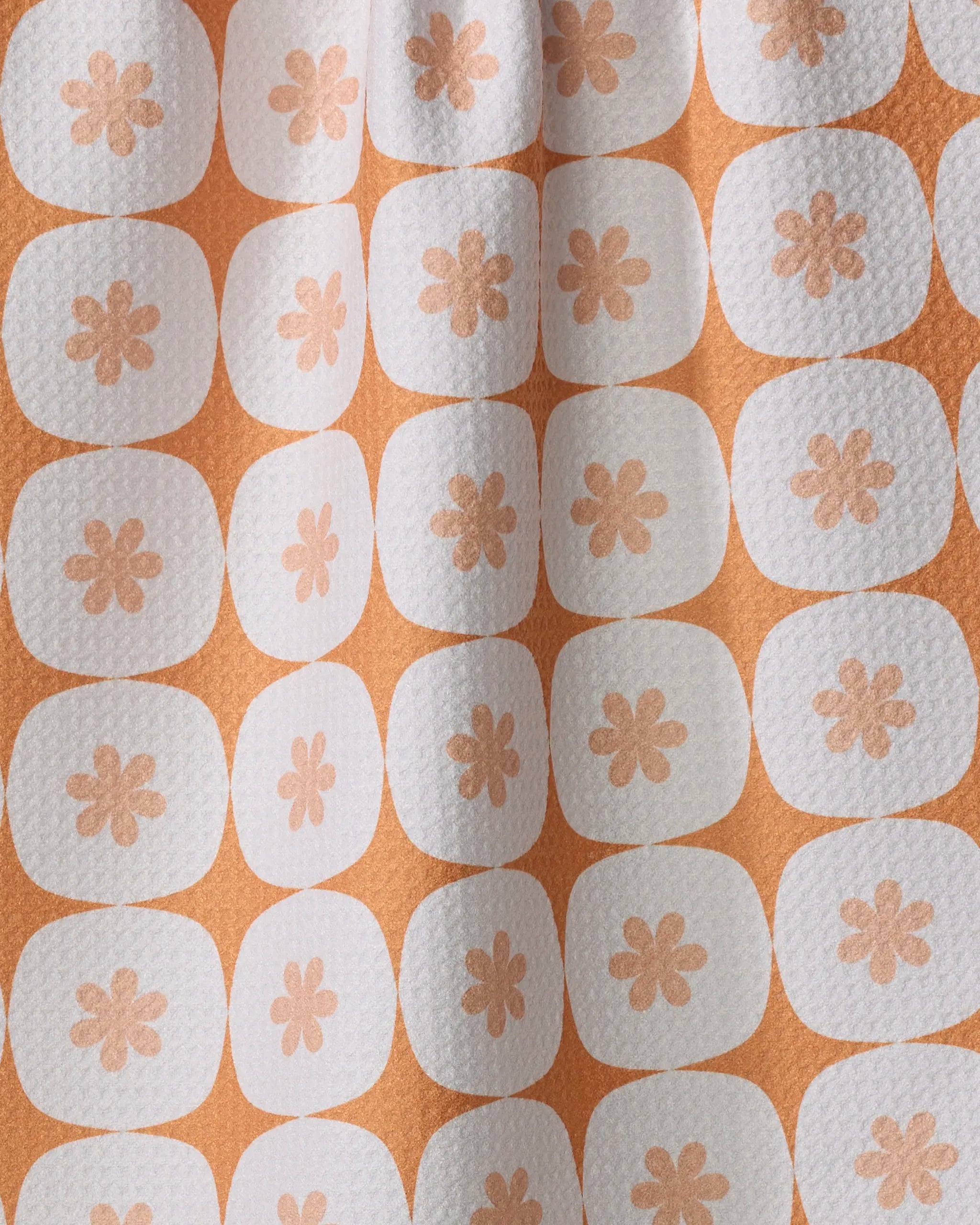 Close-up of Mindfulnice’s Flower Power tea towel: an orange, ultra-absorbent kitchen towel with a textured surface, white squares, and peach flower motifs. Subtle vertical folds add to its stylish and practical design.