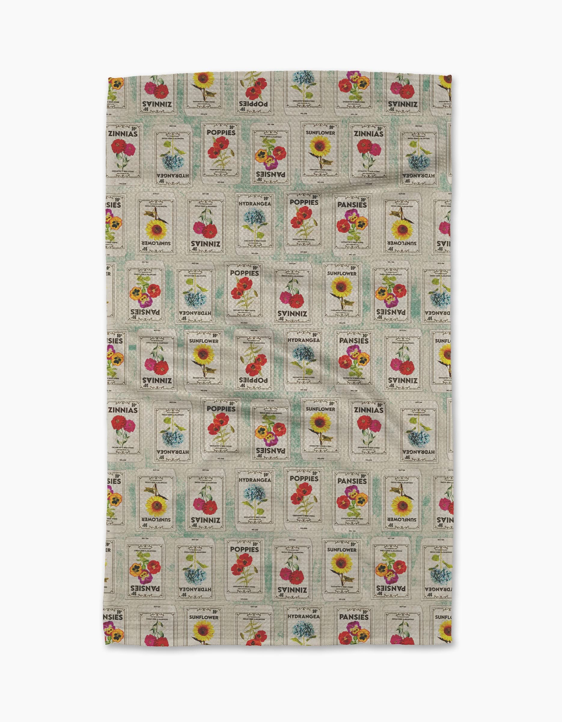 The Geometry Flower Seed Packs Tea Towel in beige features vintage-inspired tomato, poppy, sunflower, and sweet pea seed packet patterns with colorful flowers and retro text, made from ultra-absorbent recycled materials.