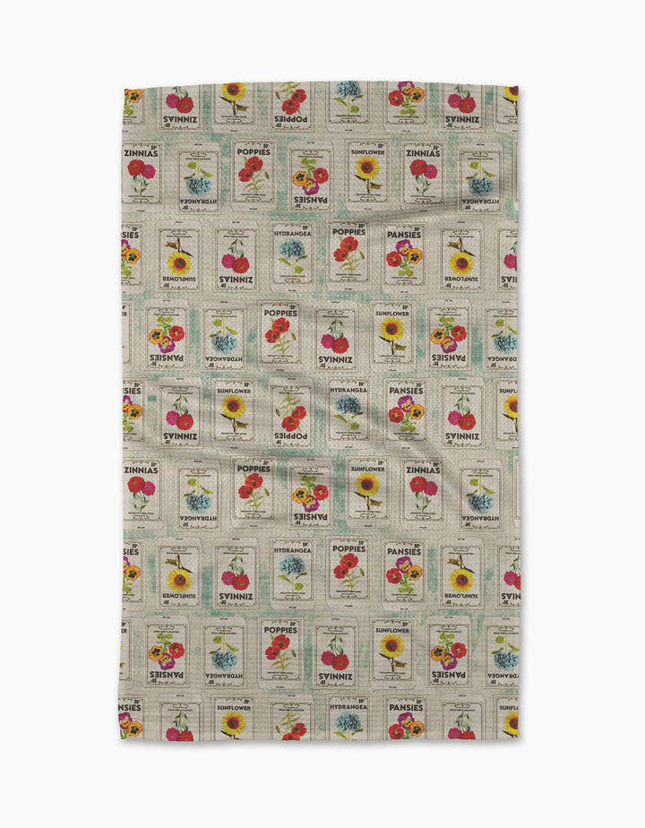 The Geometry Flower Seed Packs Tea Towel in beige features vintage-inspired tomato, poppy, sunflower, and sweet pea seed packet patterns with colorful flowers and retro text, made from ultra-absorbent recycled materials.
