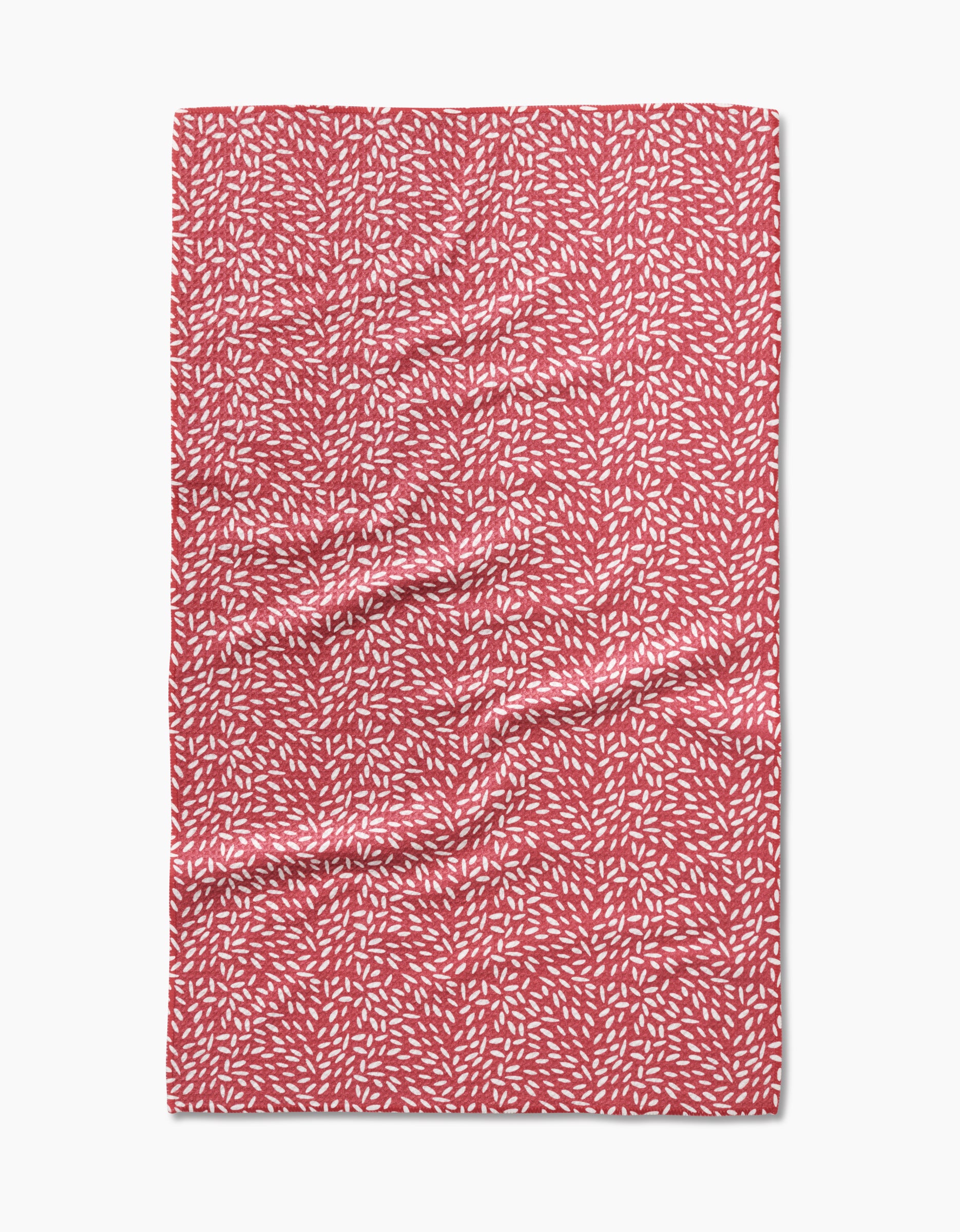 A Flower Seeds tea towel by Amita Nair, made of Geoweave fabric in red with a pattern of small white leaf-like shapes, shown laid flat with slight surface wrinkles.