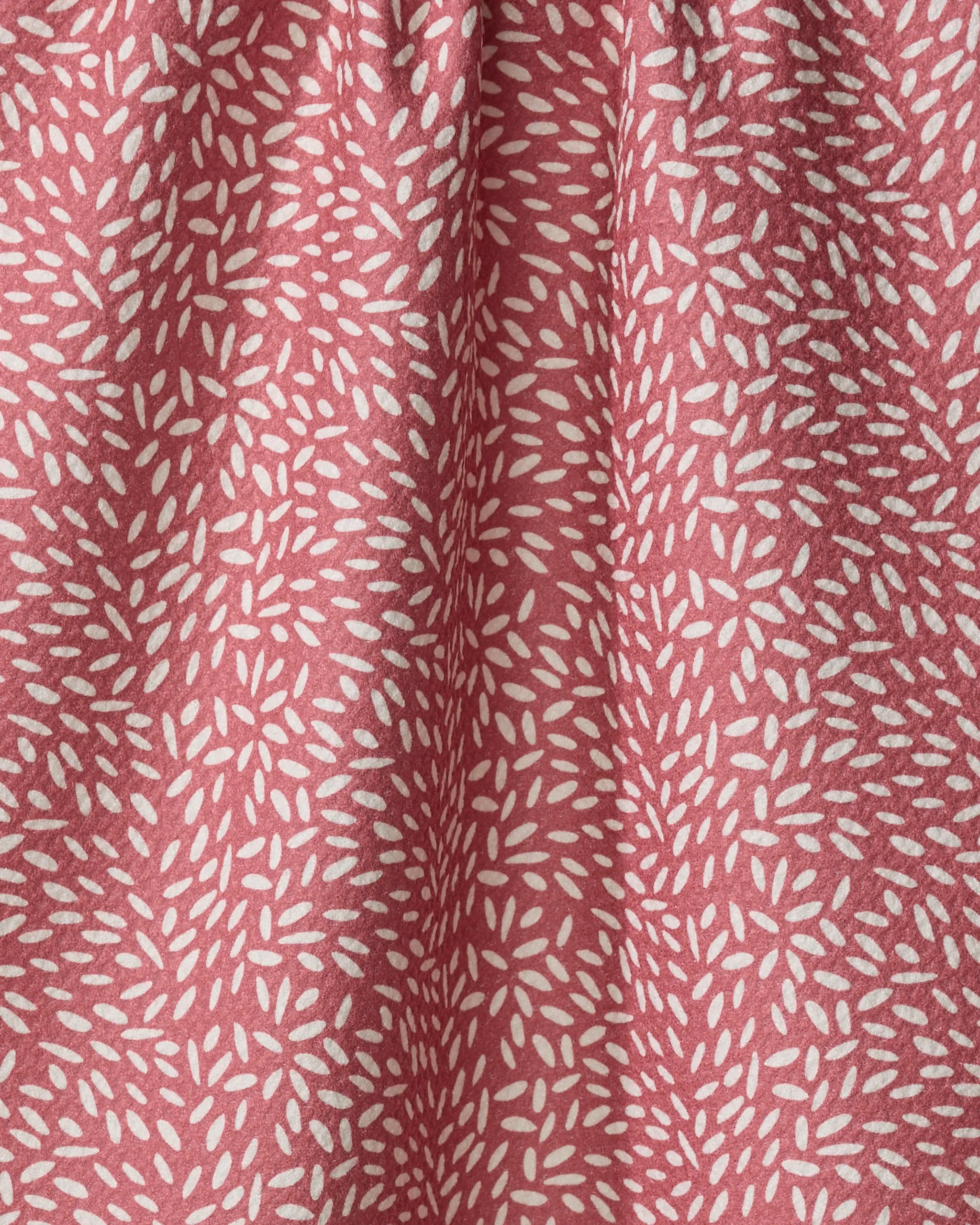 A close-up of pink packaging for Amita Nair Flower Seeds, featuring a textured surface with repeating clusters of small, white, elongated oval shapes. The soft folds and gentle shadows highlight its tactile appeal.