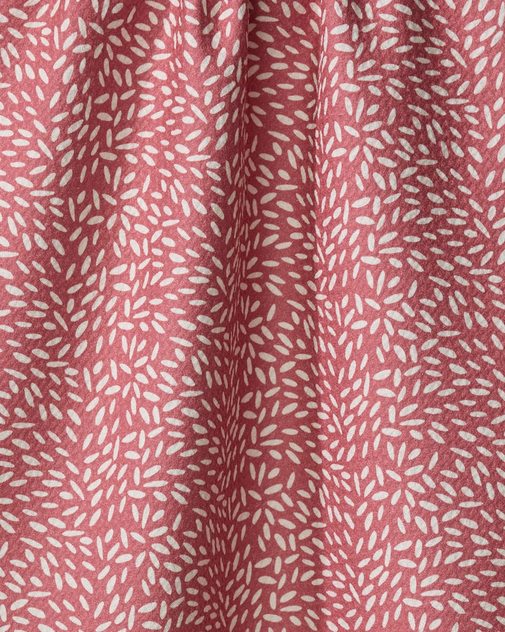 A close-up of pink packaging for Amita Nair Flower Seeds, featuring a textured surface with repeating clusters of small, white, elongated oval shapes. The soft folds and gentle shadows highlight its tactile appeal.