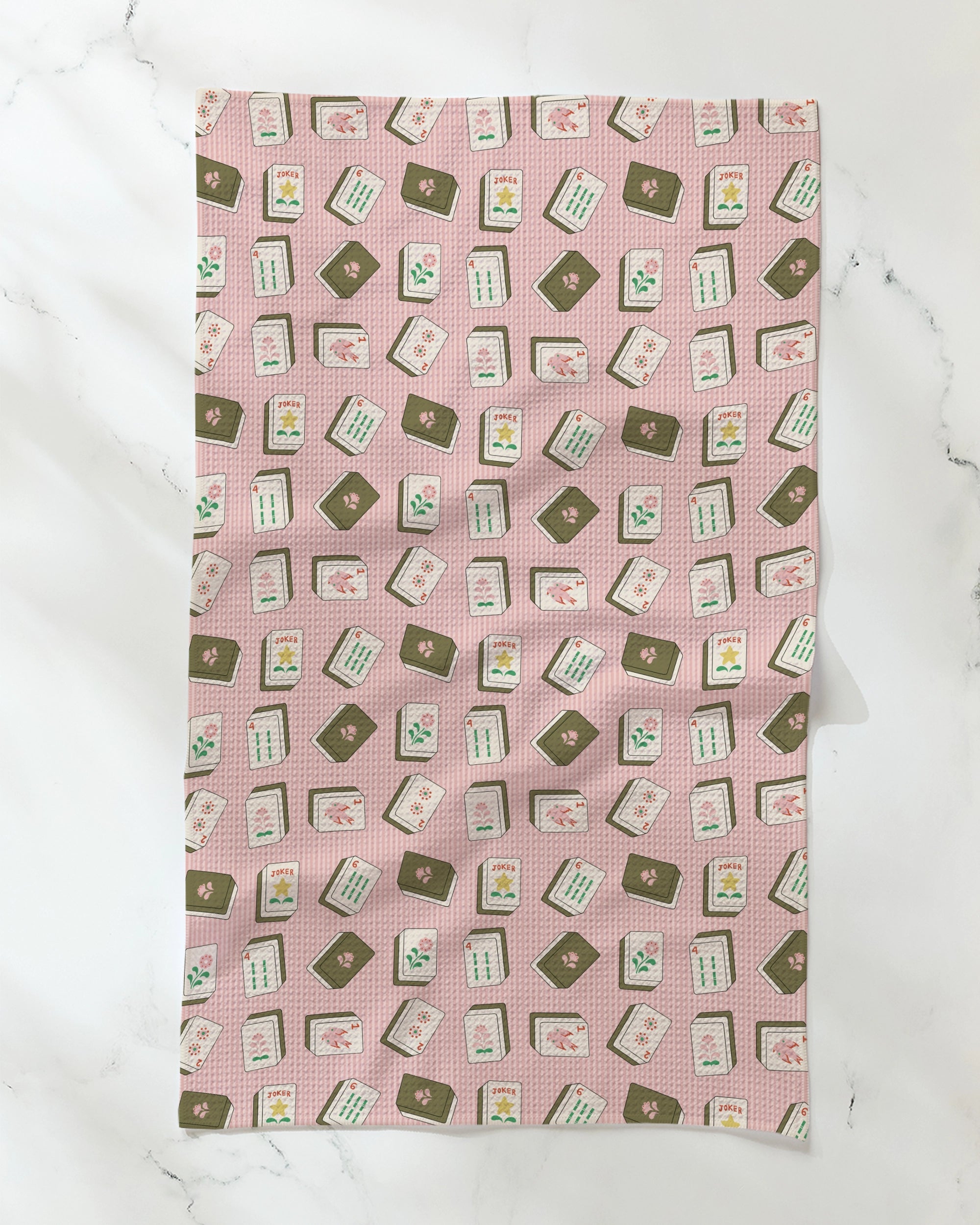 The Geometry Flower Tiles tea towel features a pink grid pattern adorned with vibrant, scattered recipe cards displaying dishes, text, and ingredients, all set against a white marble background. This absorbent towel by Geometry brings an eco-friendly and stylish flair to your kitchen while adding a playful touch.