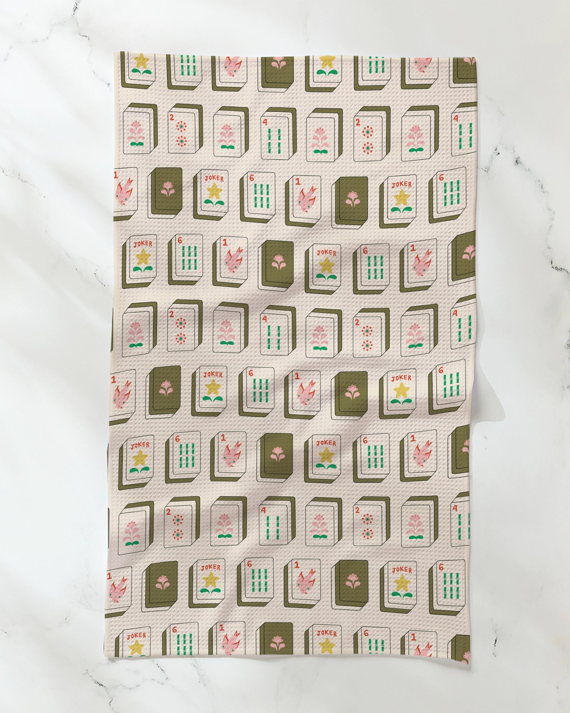 Introducing "Flower Tiles" by Geometry: a stylish and absorbent tea towel showcasing a playful mahjong tile pattern in shades of green, pink, and white on a cream background, elegantly laid flat on a marble surface. This eco-friendly tea towel brings practicality and charm to any kitchen, combining vibrant design with everyday function.