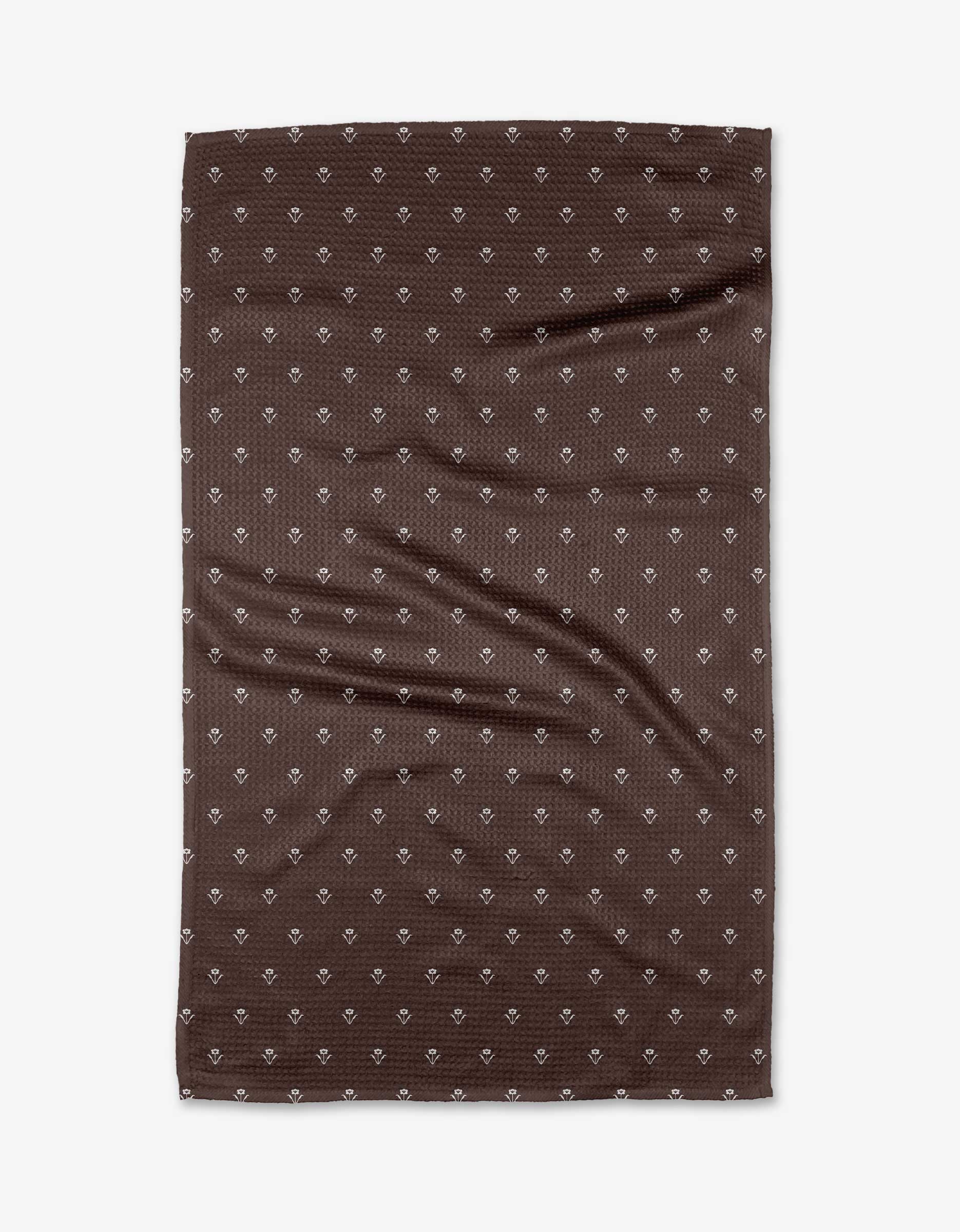 The Buy Guide’s Flowerfield Chocolate tea towel, in brown Geoweave™ fabric, displays small white diamond patterns and visible creases, shown rectangular and flat against a white background.