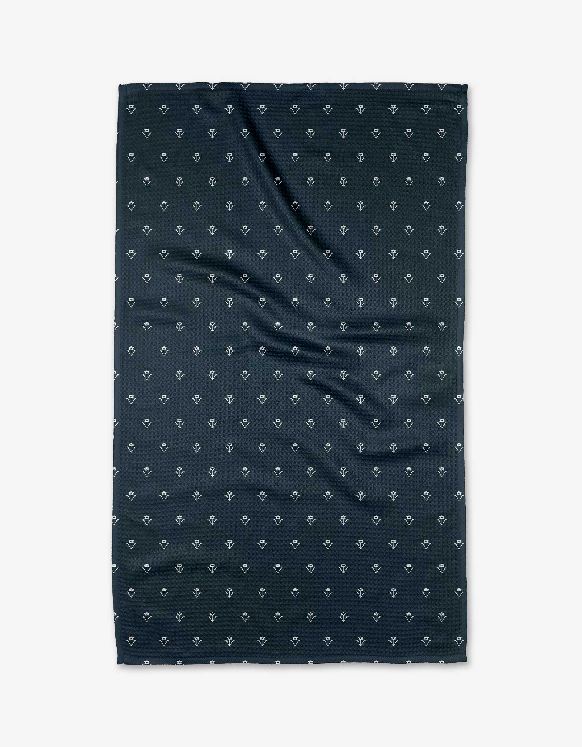 A dark navy Geoweave fabric with a subtle grid and small diamond motifs lies flat against a white background, highlighting the distinctive style of The Buy Guide’s Flowerfield Navy Tea Towel.