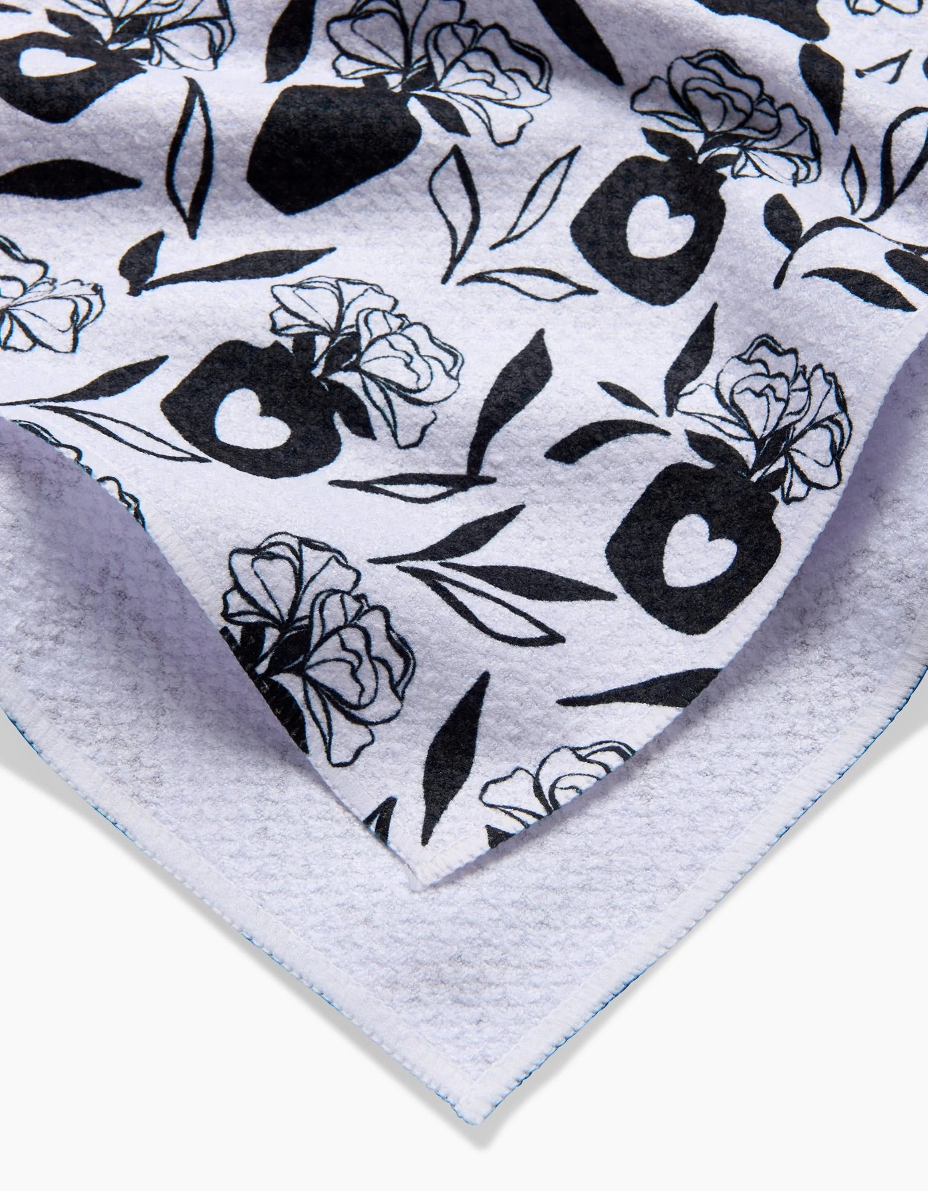 A close-up of the Flowers for Me tea towel by Charlie Rowan Designs, featuring a white background with black floral and vase patterns, including roses and hearts. The towel’s edges are neatly stitched.