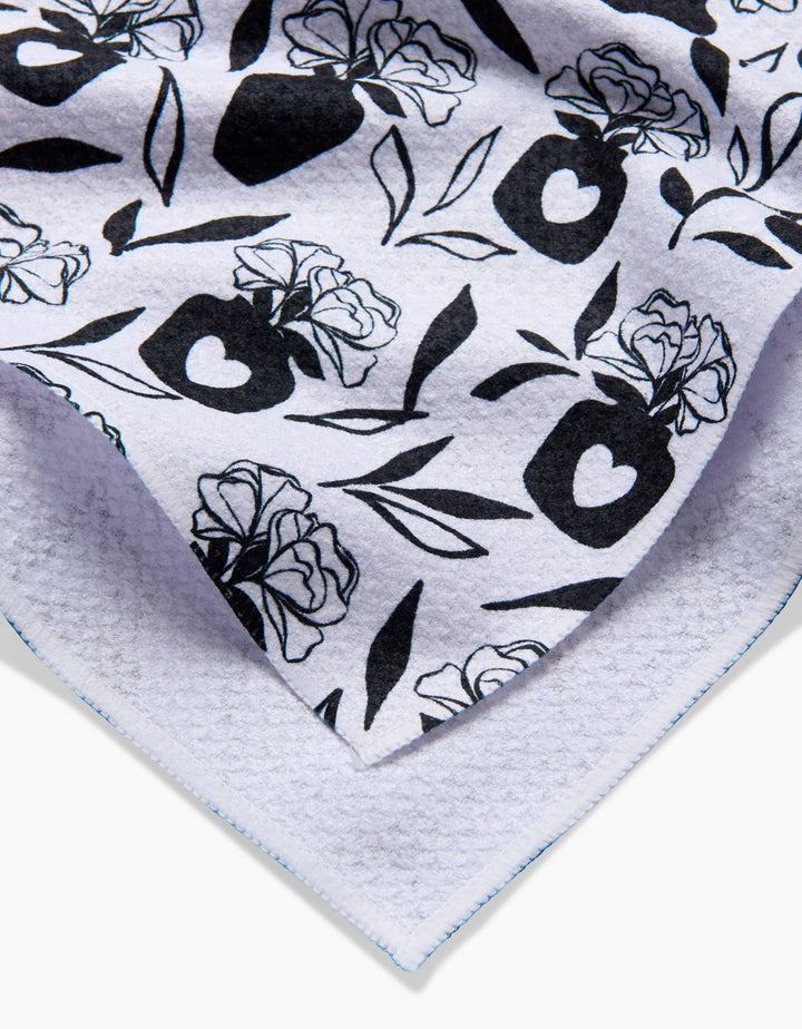 A close-up of the Flowers for Me tea towel by Charlie Rowan Designs, featuring a white background with black floral and vase patterns, including roses and hearts. The towel’s edges are neatly stitched.
