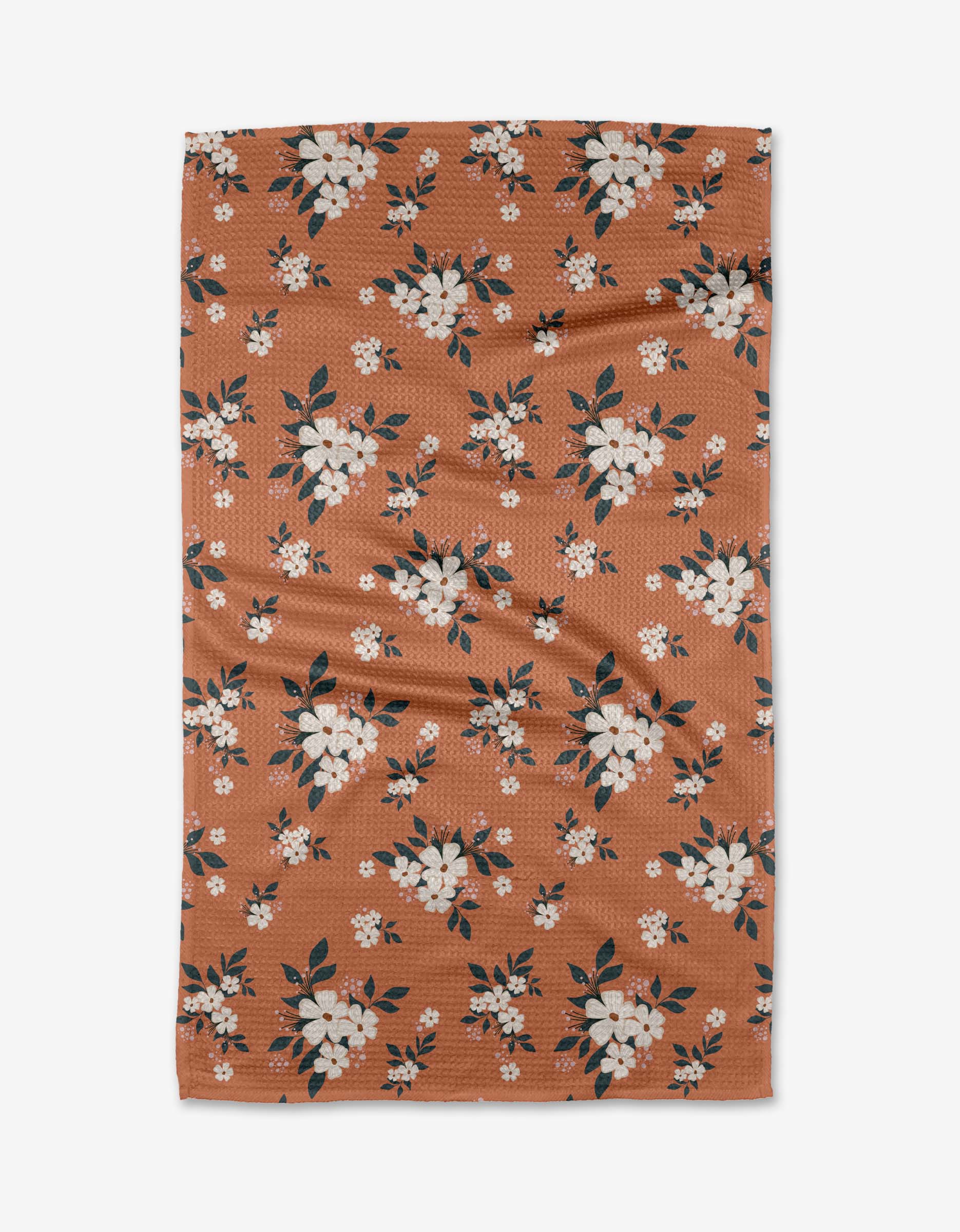 The Flowers in the Field tea towel by Charlie Rowan Designs is a rectangular brown towel with white and pink floral patterns and dark green leaves, crafted from recycled materials and shown flat on a white background.