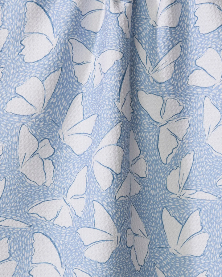 The Hufton Studio Fly Away Butterfly dish towel features a light blue color with white butterflies and delicate dots. Softly folded, it combines whimsical charm and practical absorbency, perfect for brightening any kitchen.