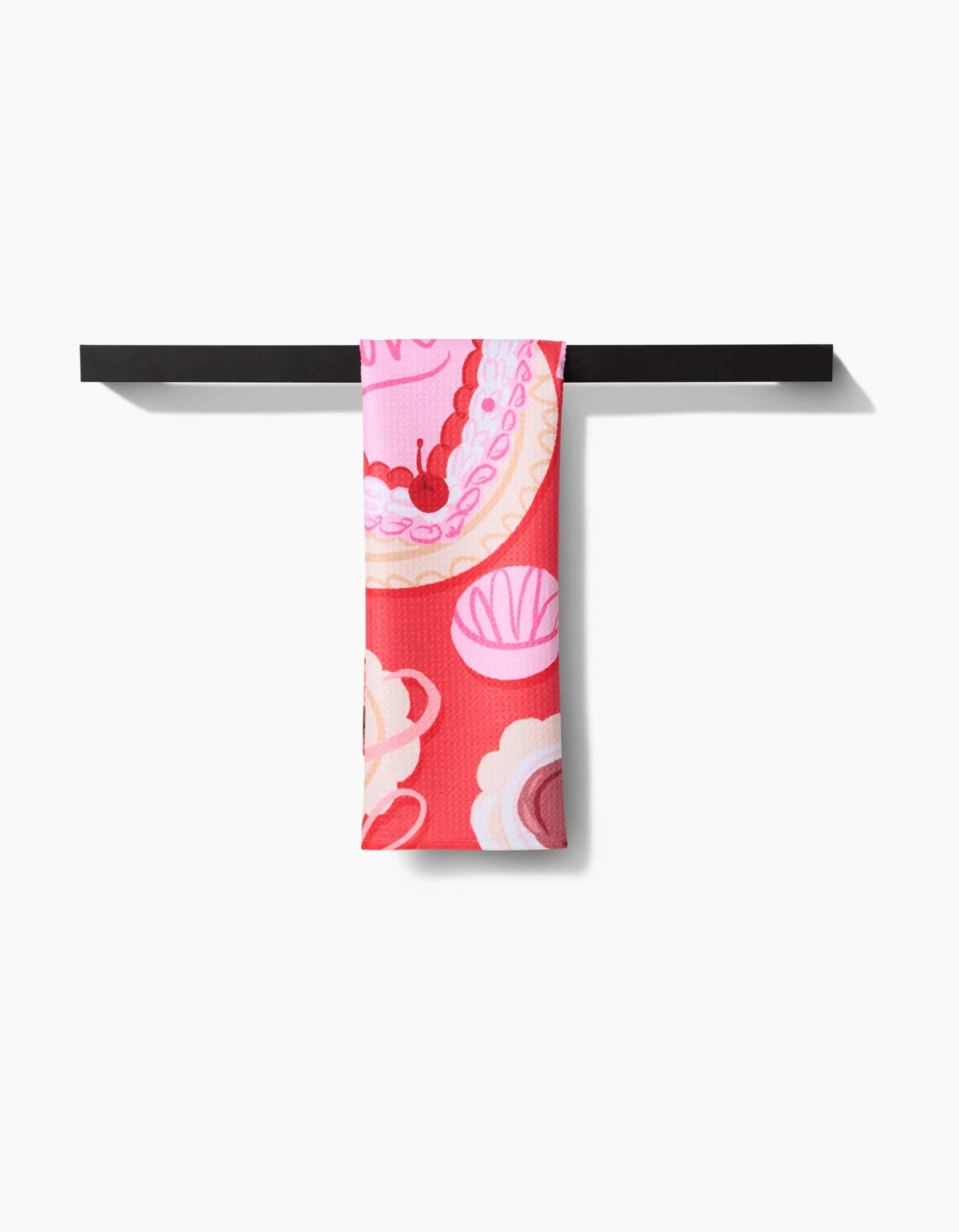 The Food of Love tea towel by Janna Sue Design features bold pink and red abstract florals. Made from ultra-absorbent recycled materials, it’s draped over a black bar against a white background.